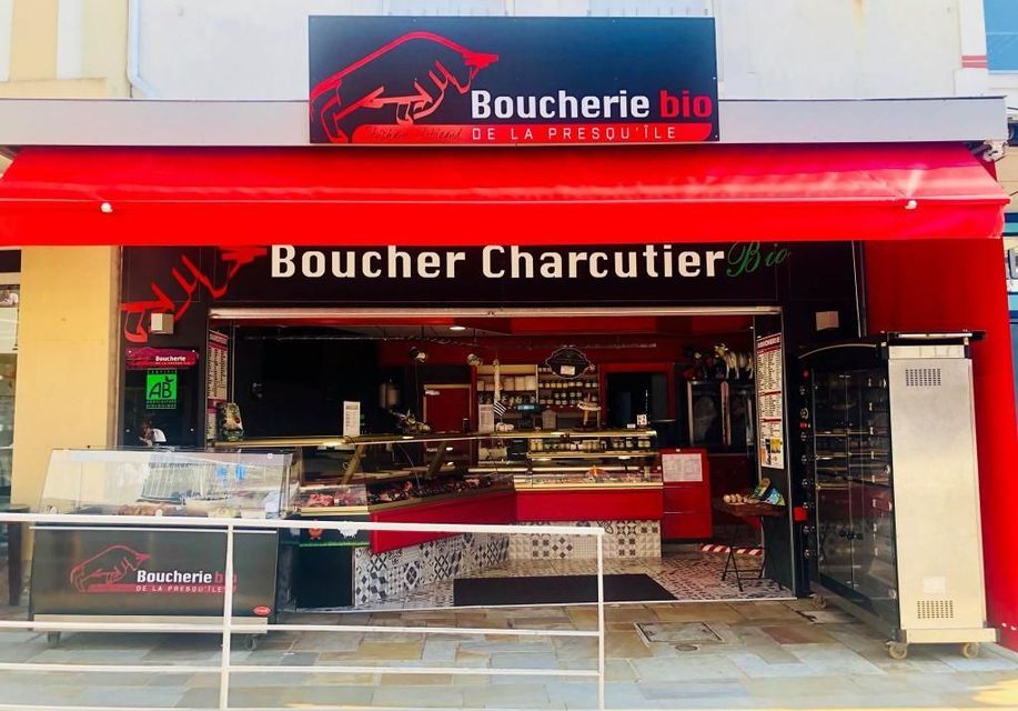 Façade de boucherie avec auvent rouge et comptoir d'exposition, portant les inscriptions Boucherie et boucher-charcutier.