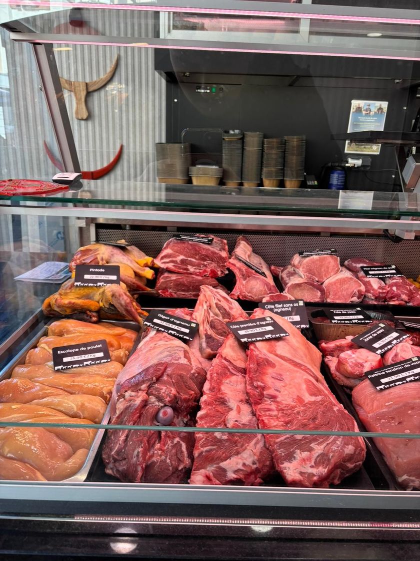 Vitrine de boucherie présentant un assortiment de viandes crues et de morceaux étiquetés sur des plateaux métalliques.
