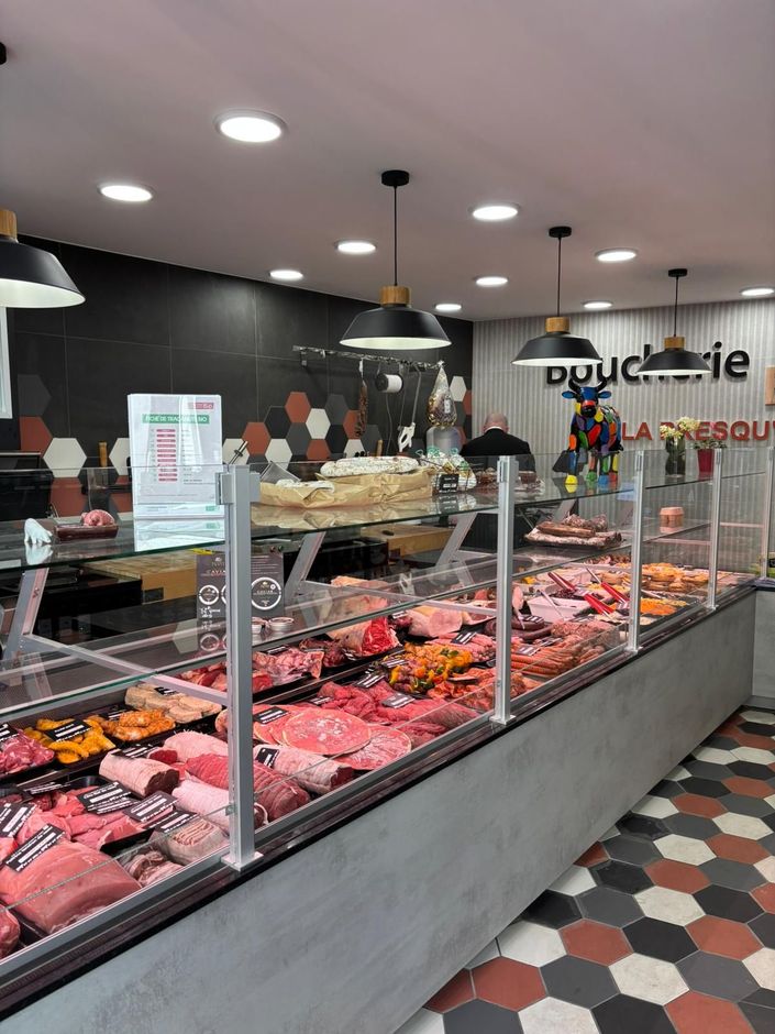 Comptoir de boucherie avec plateaux de viande sous vitrine, sol carrelé et luminaires suspendus.
