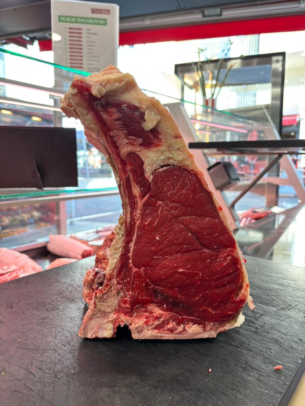 Côte de bœuf crue dressée sur une planche à découper noire dans la vitrine d'une boucherie