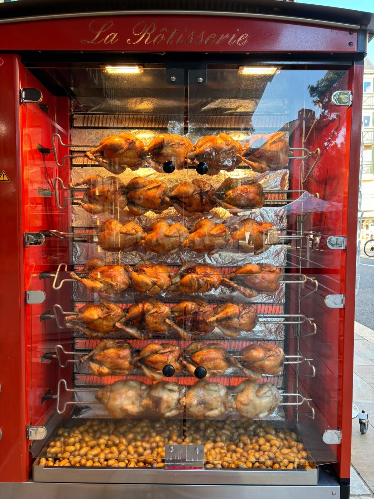 Vitrine rouge présentant des poulets rôtis, avec plusieurs poulets et plateaux en dessous.