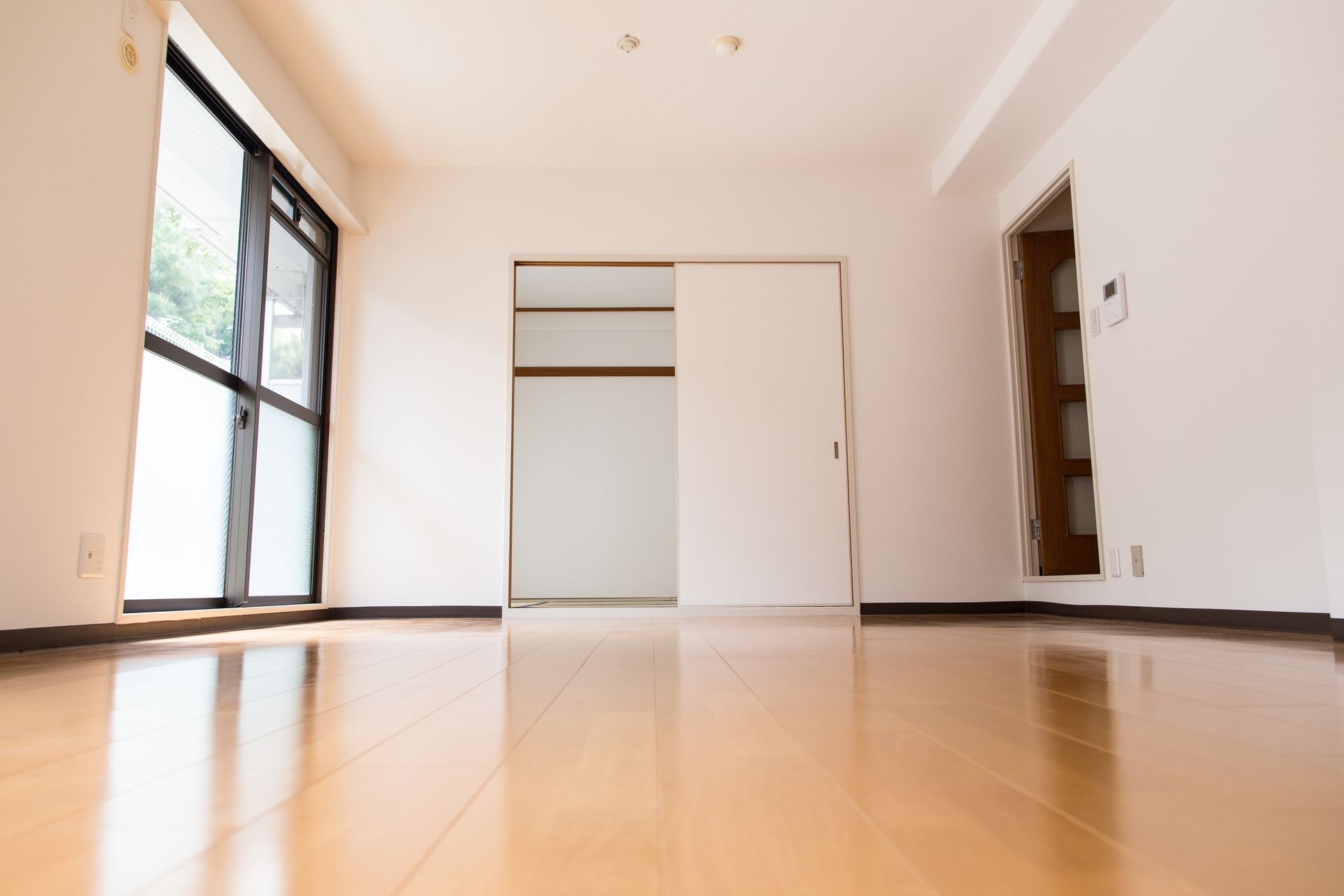 Pièce vide avec parquet, portes de placard coulissantes et grande fenêtre.