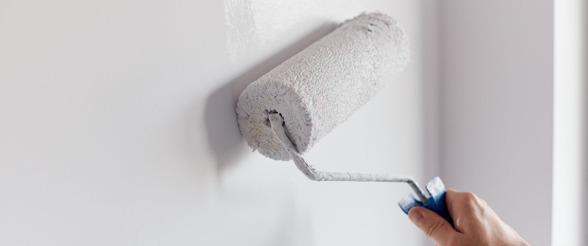 La main d'une personne utilisant un rouleau à peinture sur un mur blanc.