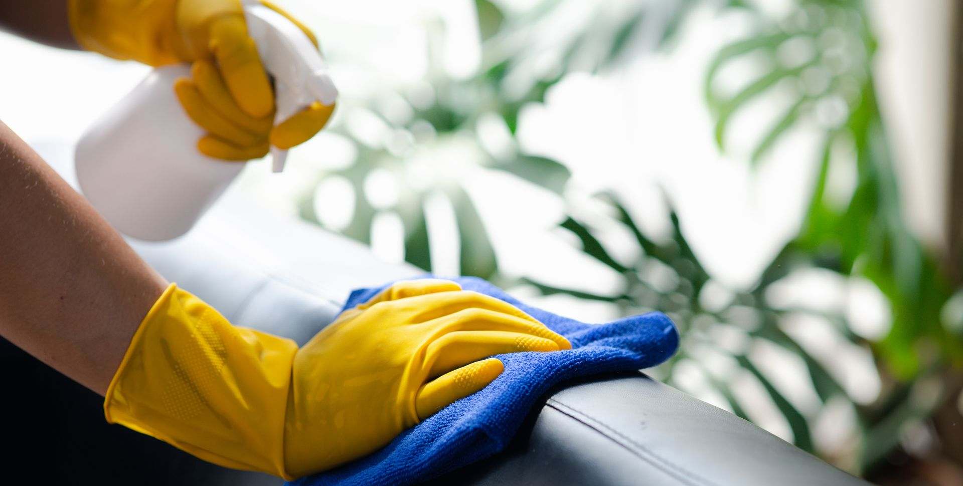 Une personne portant des gants jaunes vaporise et essuie une surface avec un chiffon bleu.