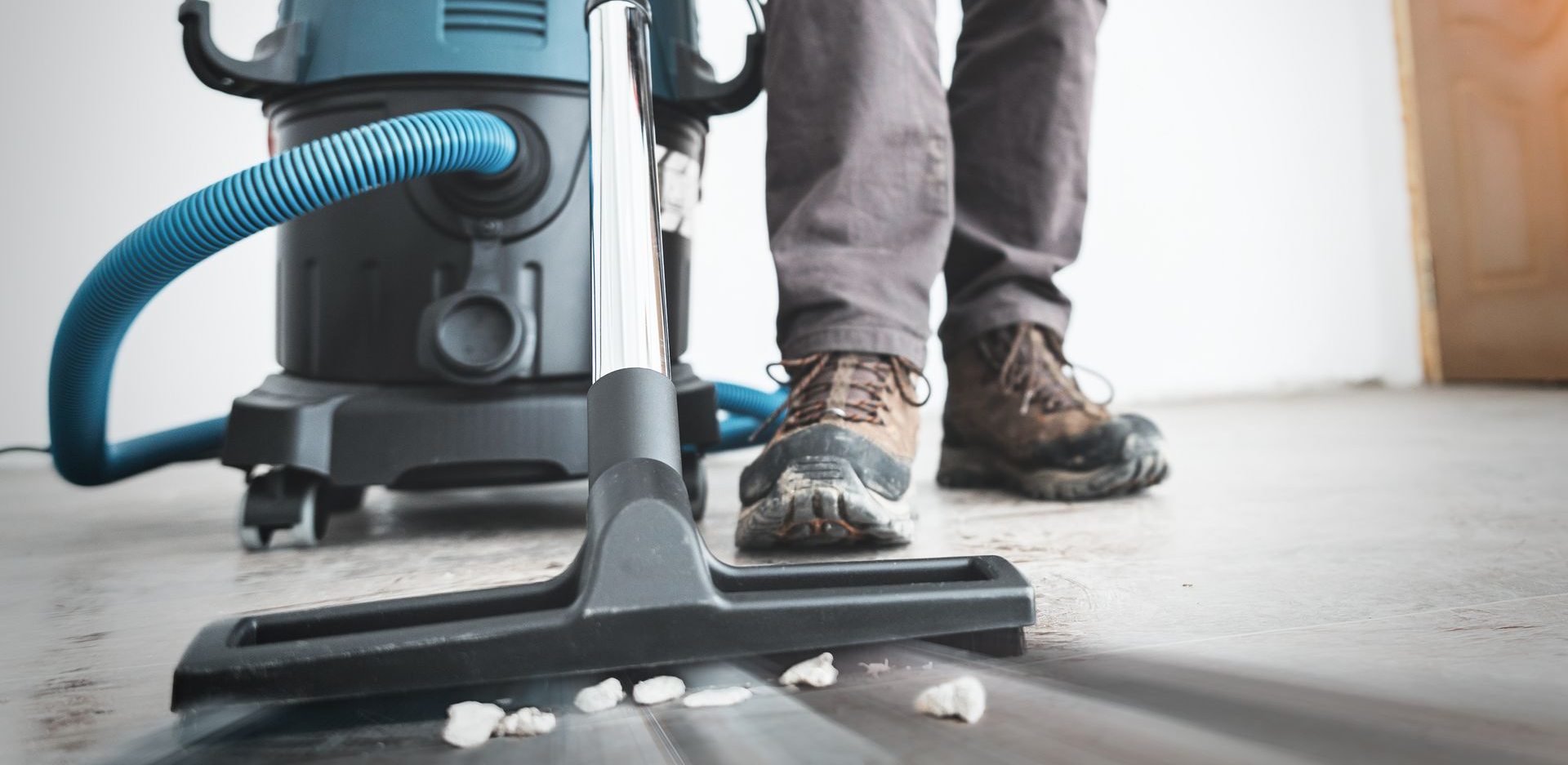 Une personne passant l'aspirateur sur un sol en béton avec un aspirateur bleu.