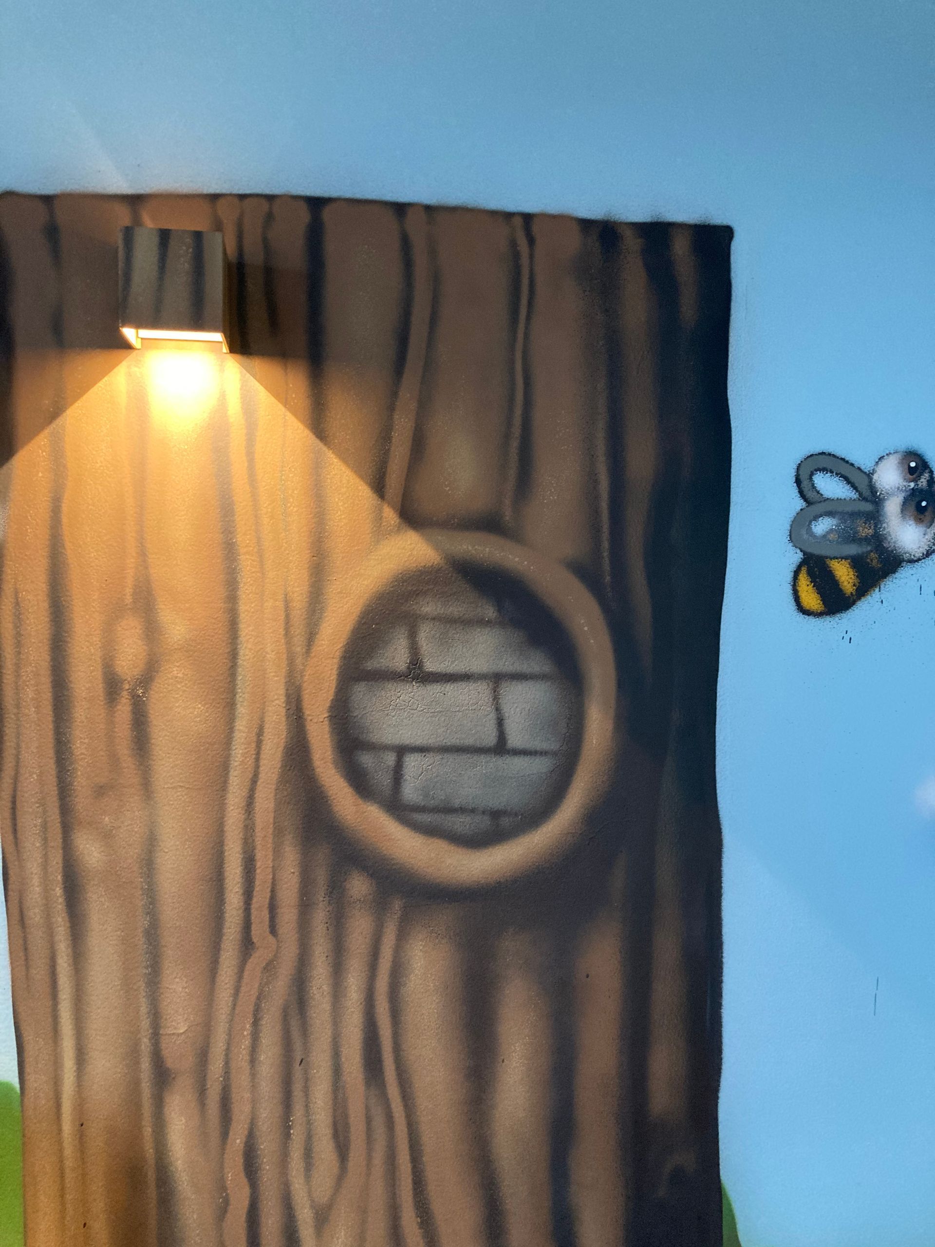 Tronc d'arbre peint avec une abeille et une applique allumée sur le mur