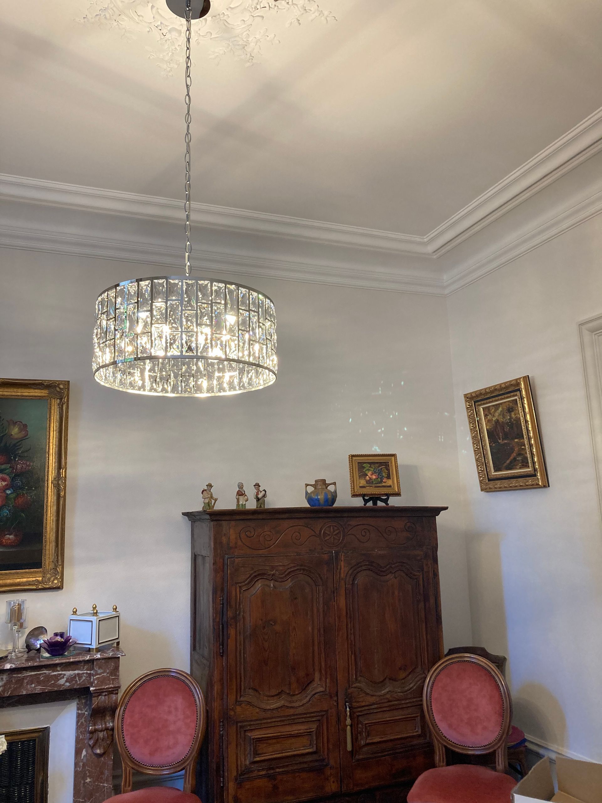 Pièce avec des moulures au plafond, de nombreux cadres aux murs et un lustre brillant