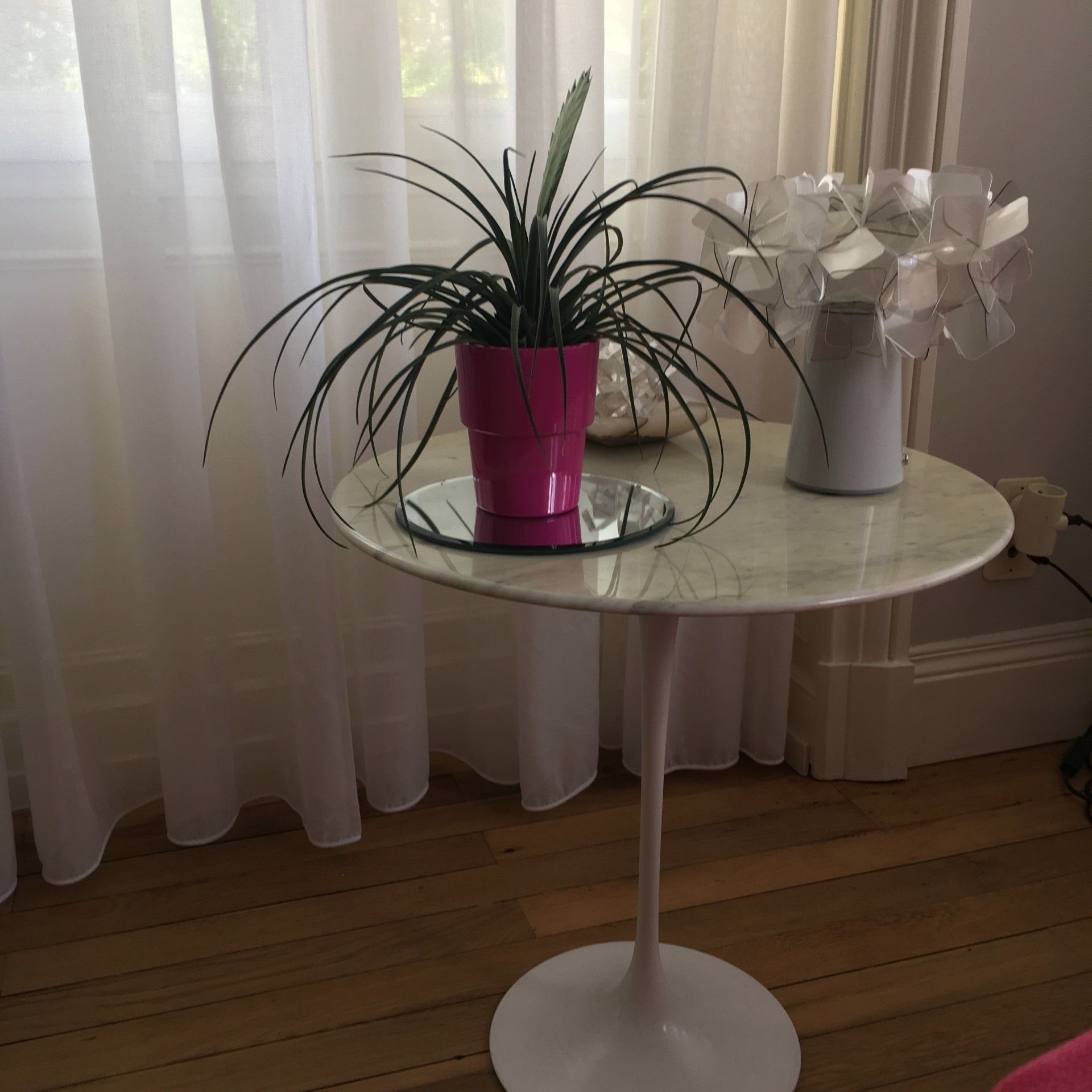 Lampe sur une petite table et une plante dans un pot rose à côté