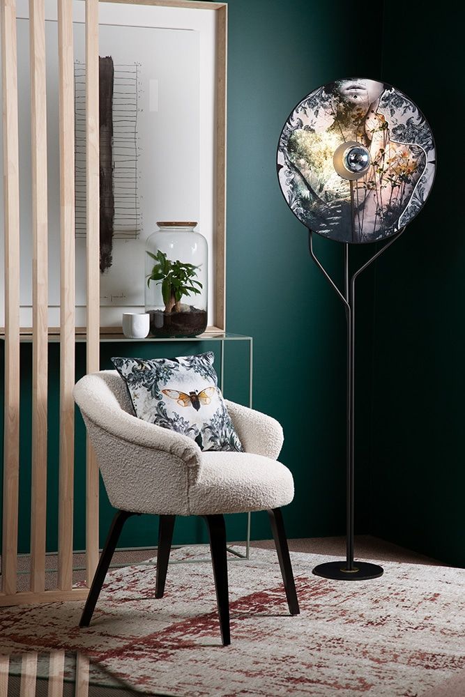 Lampadaire face à un mur vert foncé à côté d'un fauteuil blanc