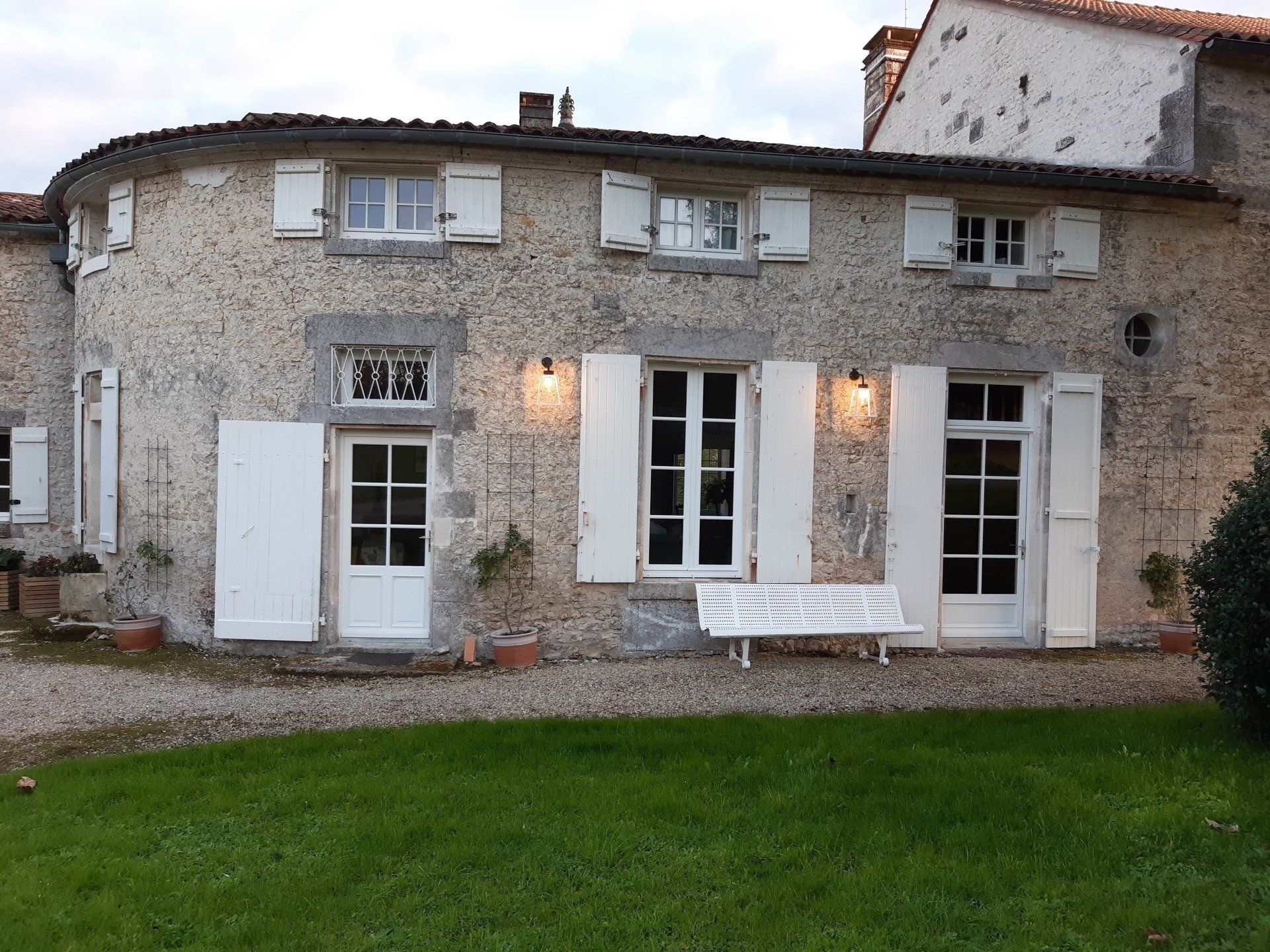 Façade extérieure d'une maison en pierres apparentes avec des volets blancs