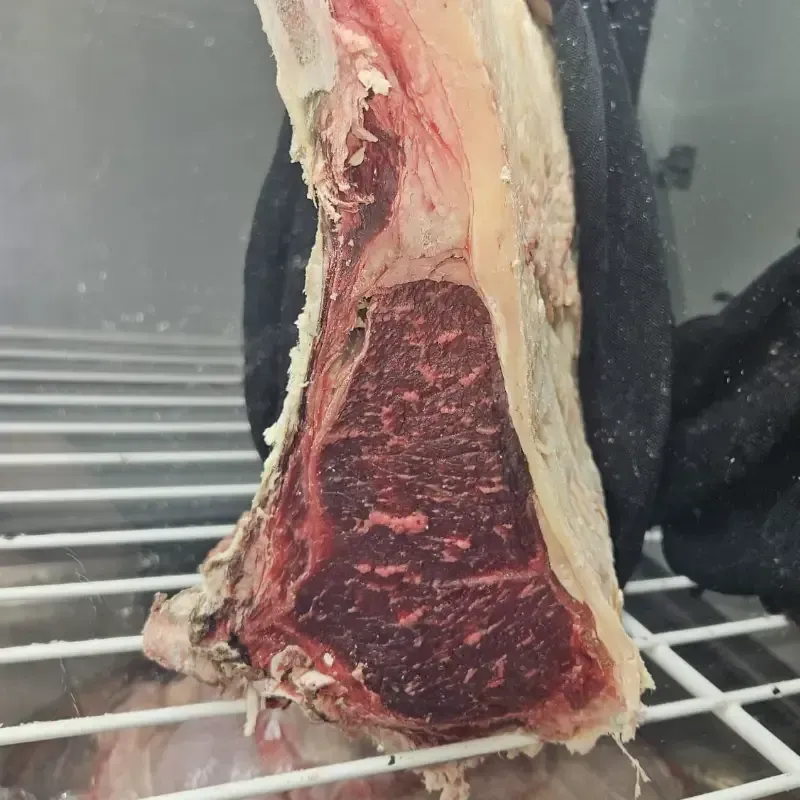 Un gran trozo de carne cruda, con vetas de grasa visibles y una capa de grasa, que reposa sobre una rejilla metálica