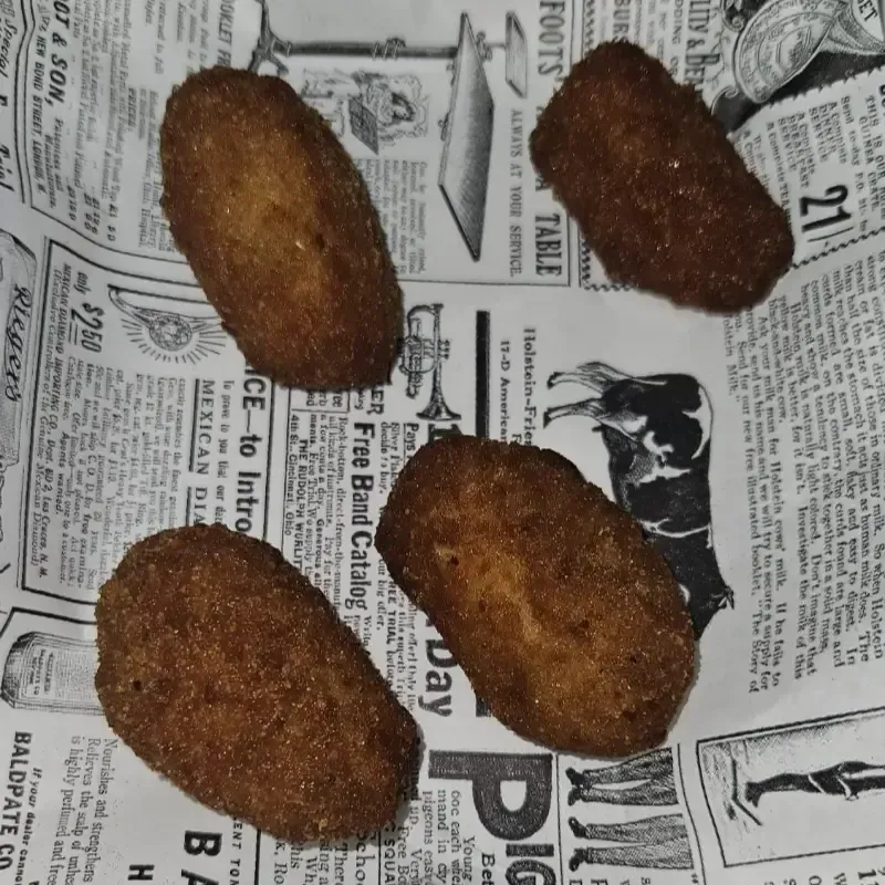 Cuatro croquetas, dispuestas sobre una superficie cubierta con imágenes de periódicos antiguos en blanco y negro.