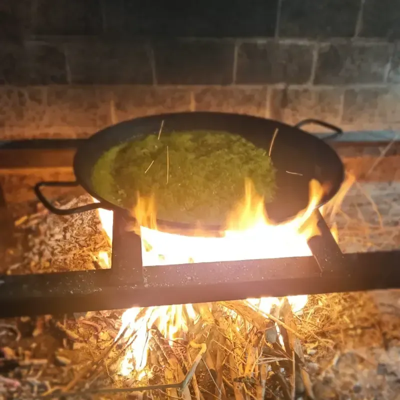 Una paellera cocinándose sobre fuego de leña en una chimenea de piedra.