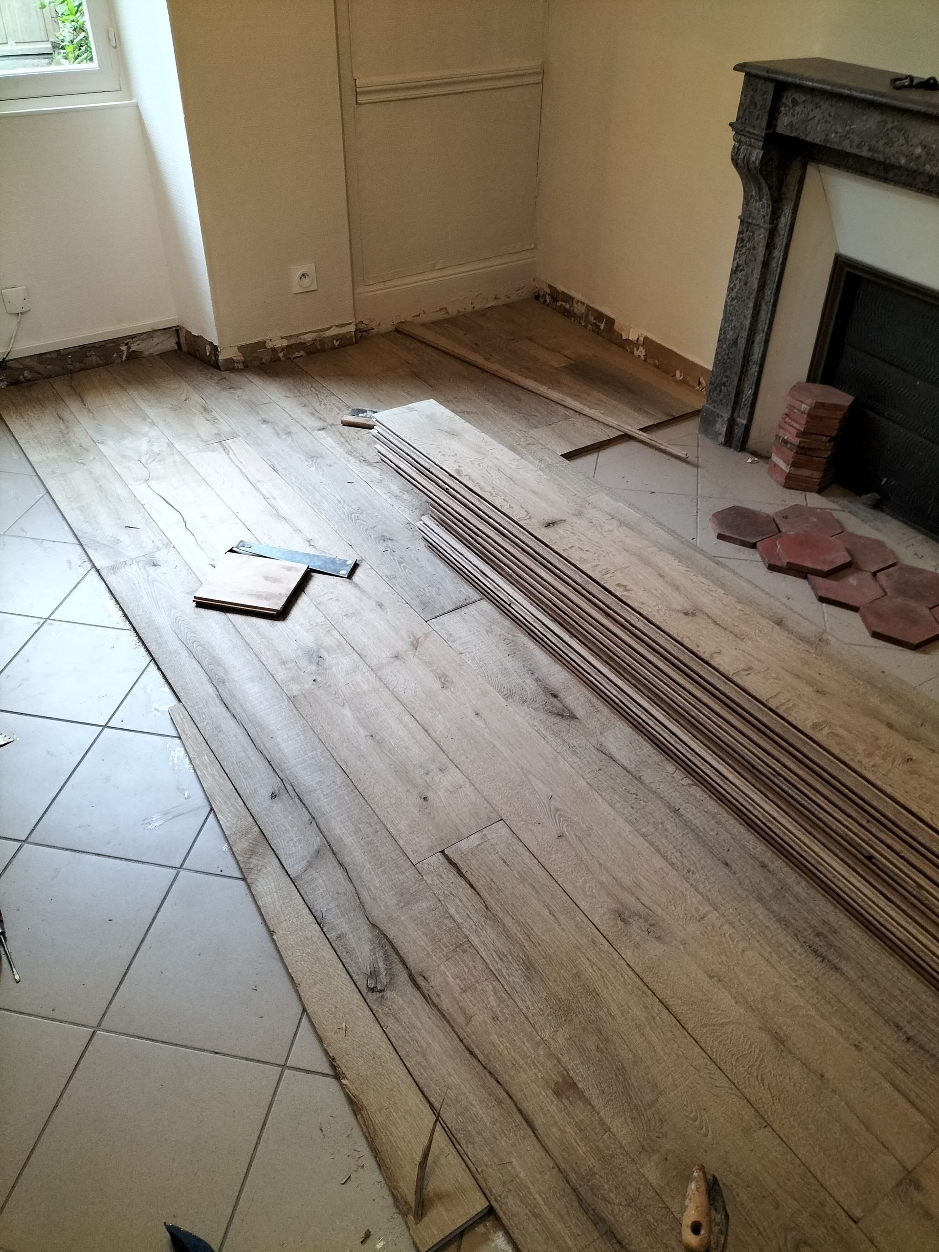 Pose de parquet dans une pièce avec cheminée et carrelage.