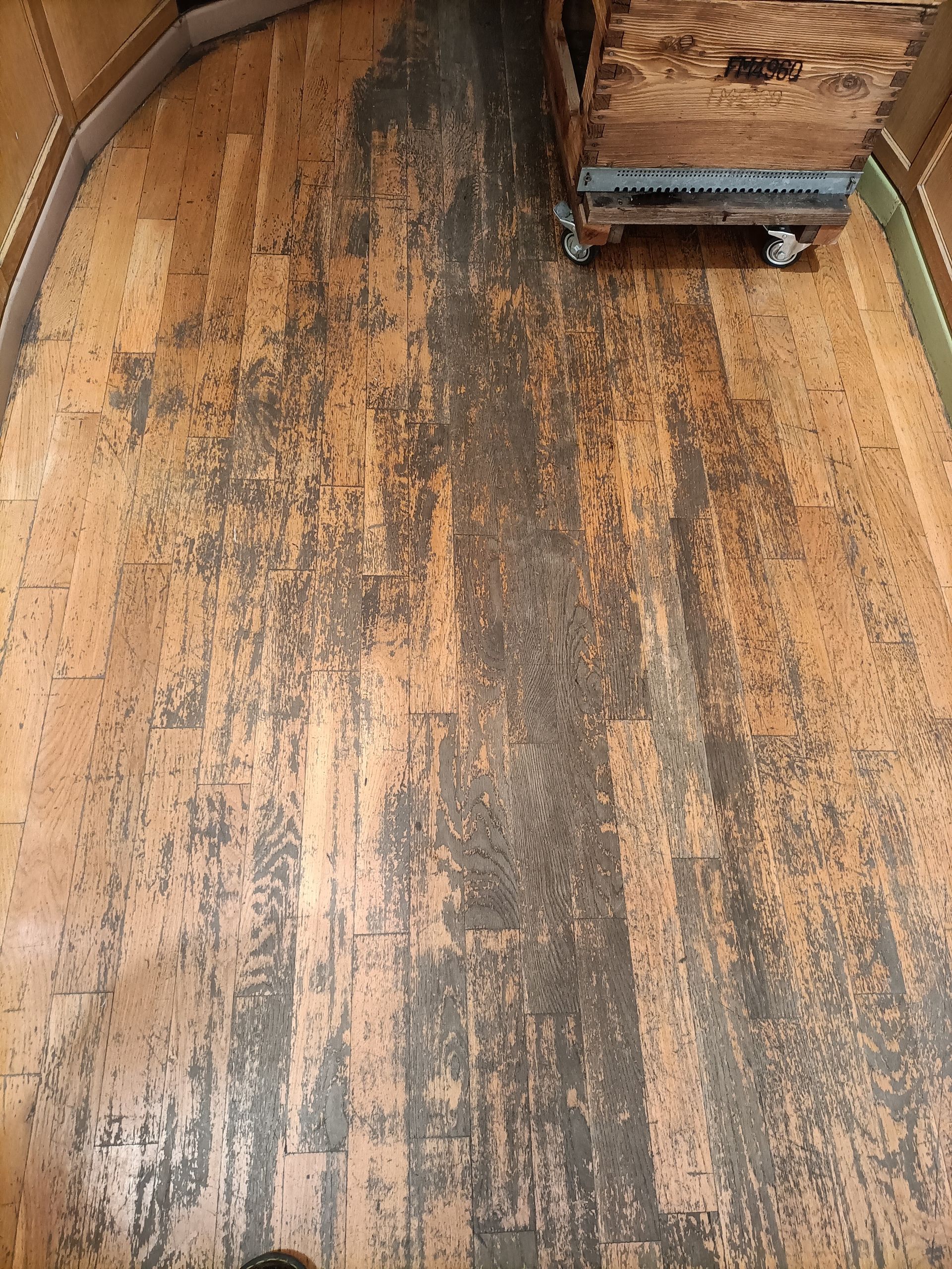 Parquet usé avec des zones sombres et abîmées, jouxtant un meuble en bois finement travaillé.