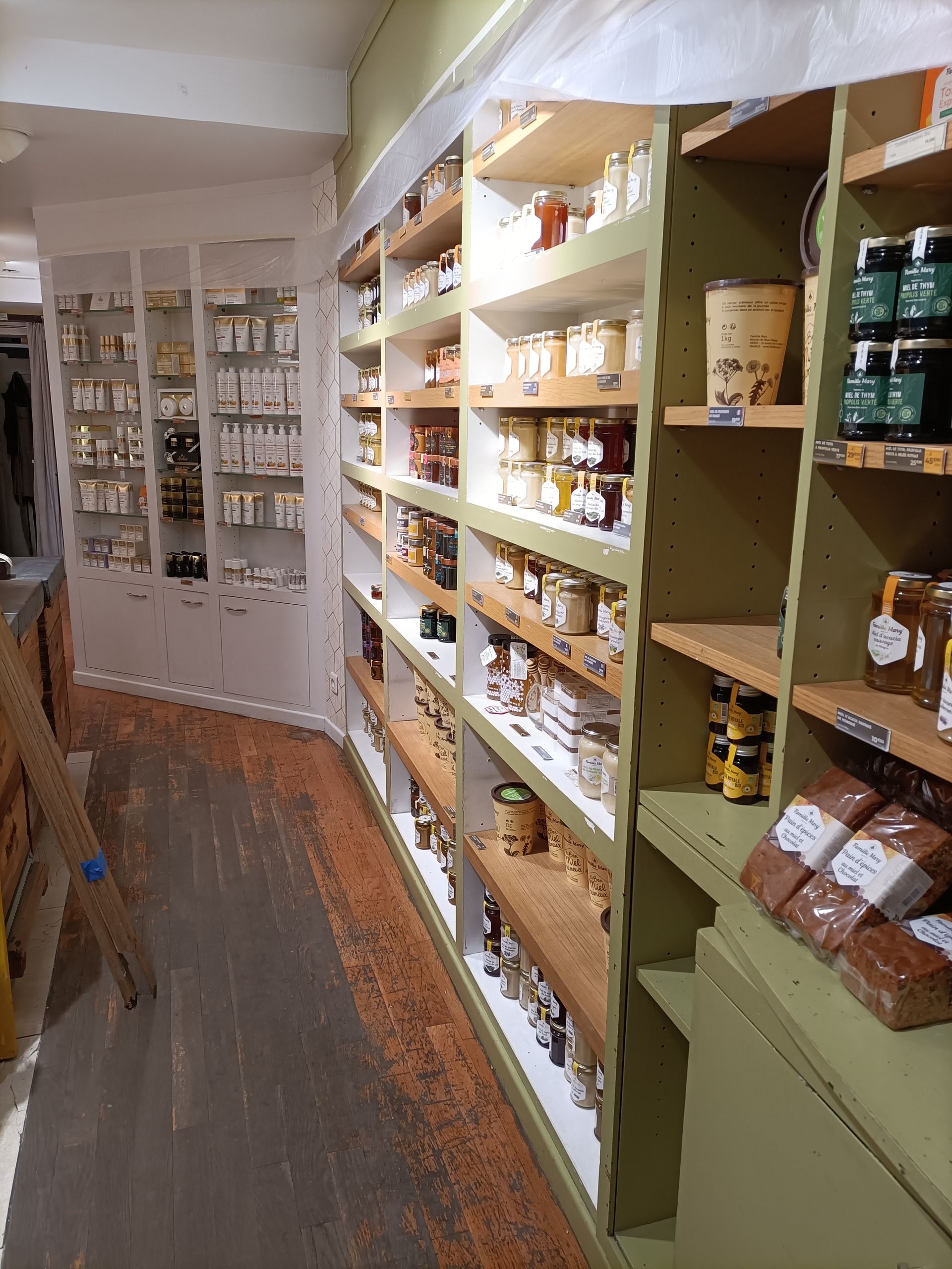 Des étagères d'un magasin, remplies de bocaux et d'emballages peints en vert clair, longent un sol en bois.