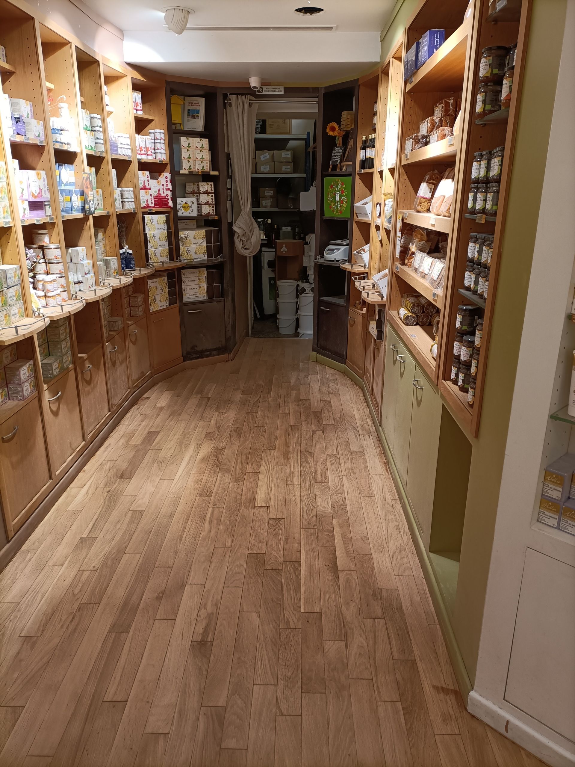 Allée étroite d'un magasin avec des étagères en bois remplies de produits ; sol en bois.