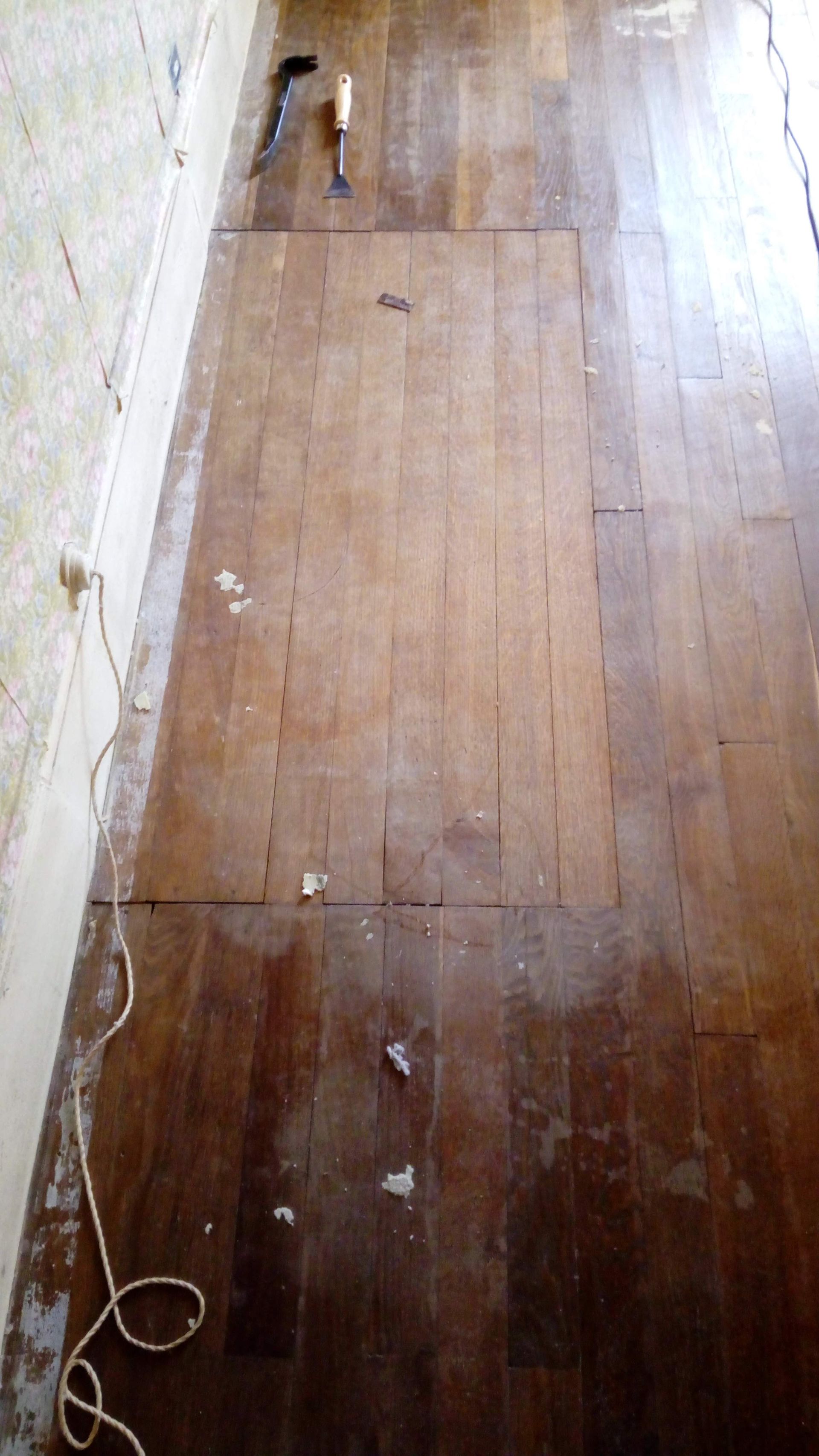 Plancher en bois avec des planches manquantes, des outils et des débris éparpillés.