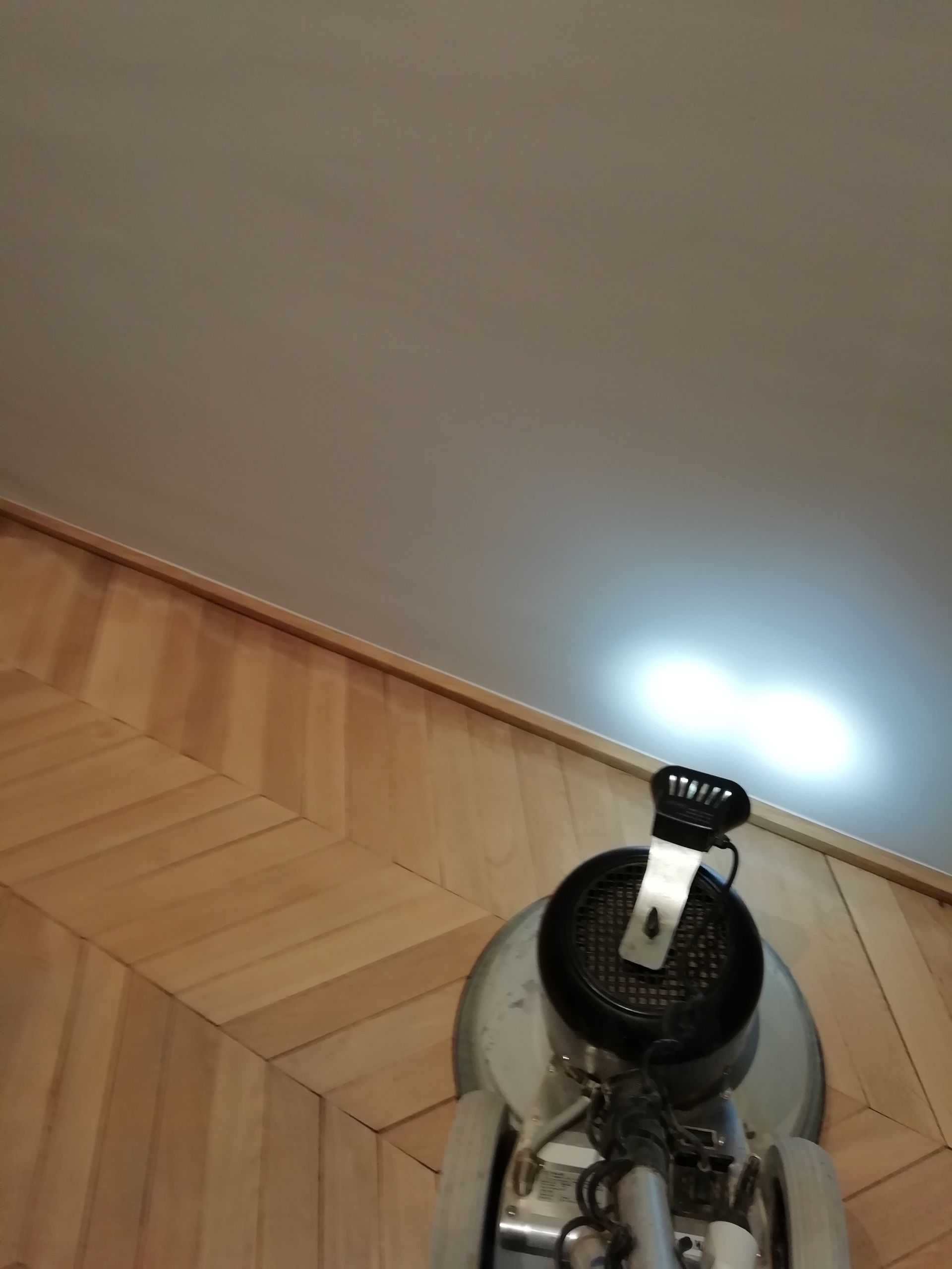 Ponceuse à parquet sur un plancher en bois franc, vue de dessus. La lumière éclaire la machine et le plafond.