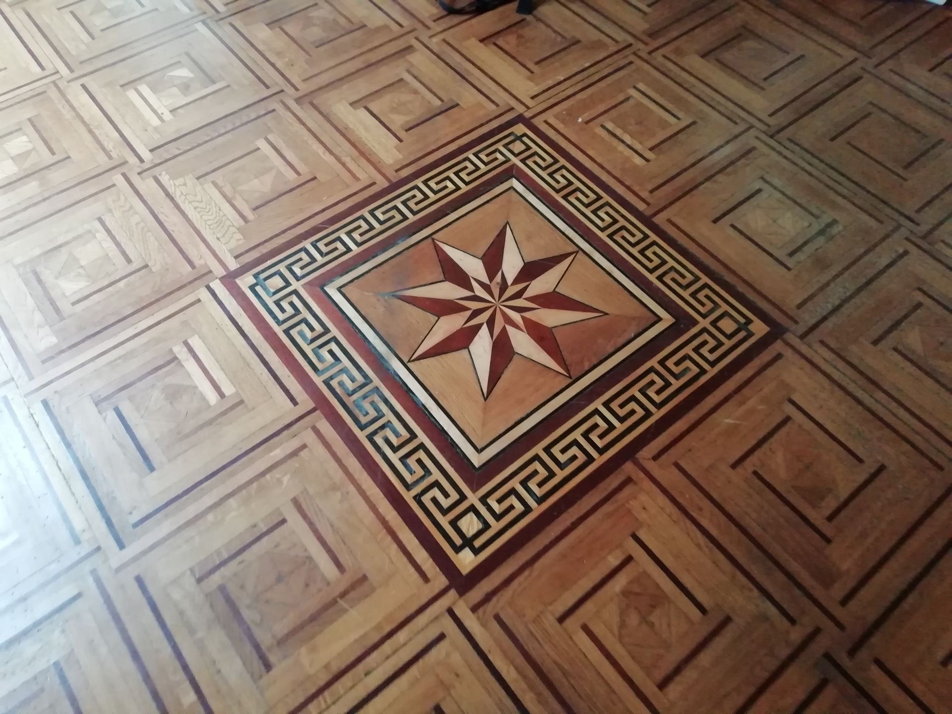 Parquet en bois avec incrustations en forme d'étoile et bordure à motif grec.
