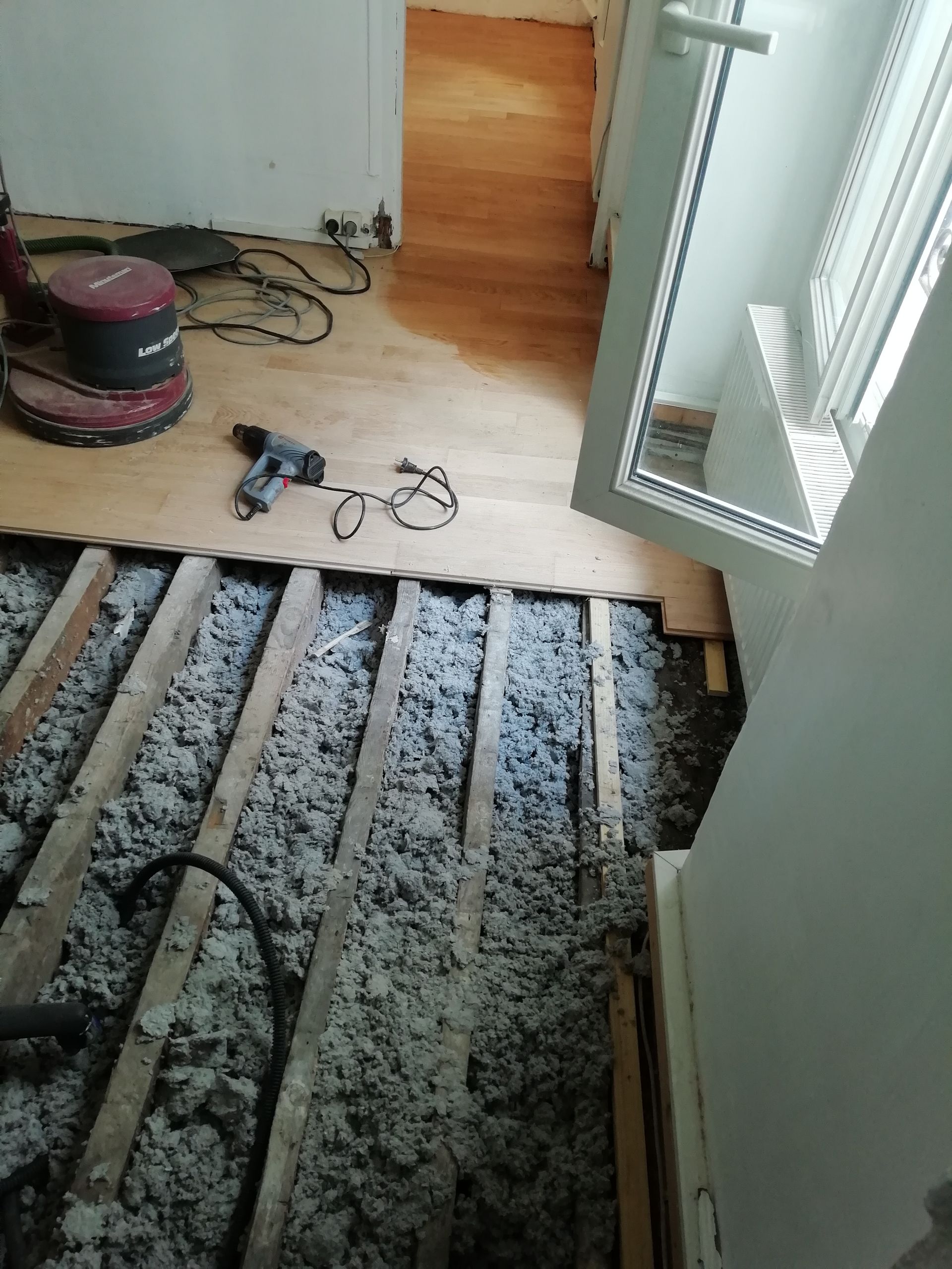 Rénovation du plancher : solives apparentes avec isolation, plancher en bois, outils et fenêtre ouverte.