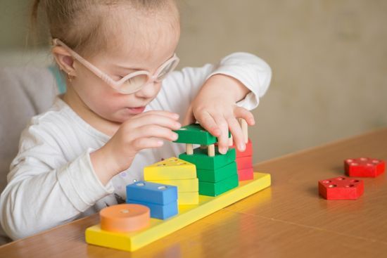 Mädchen mit Brille baut mit Bauklötzen, um die Feinmotorik zu stärken