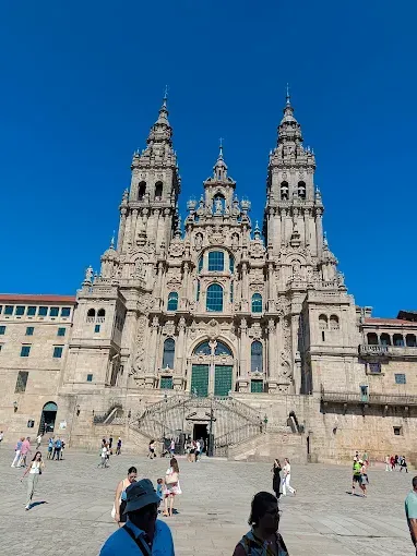 Fachada de la catedral con torres gemelas y escalinatas bajo un cielo azul brillante, con gente caminando frente a ella.