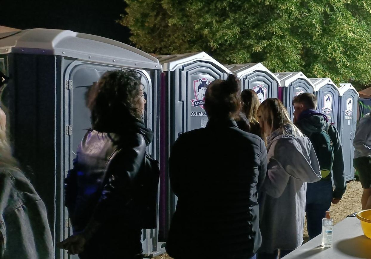 Des gens font la queue devant des toilettes mobiles