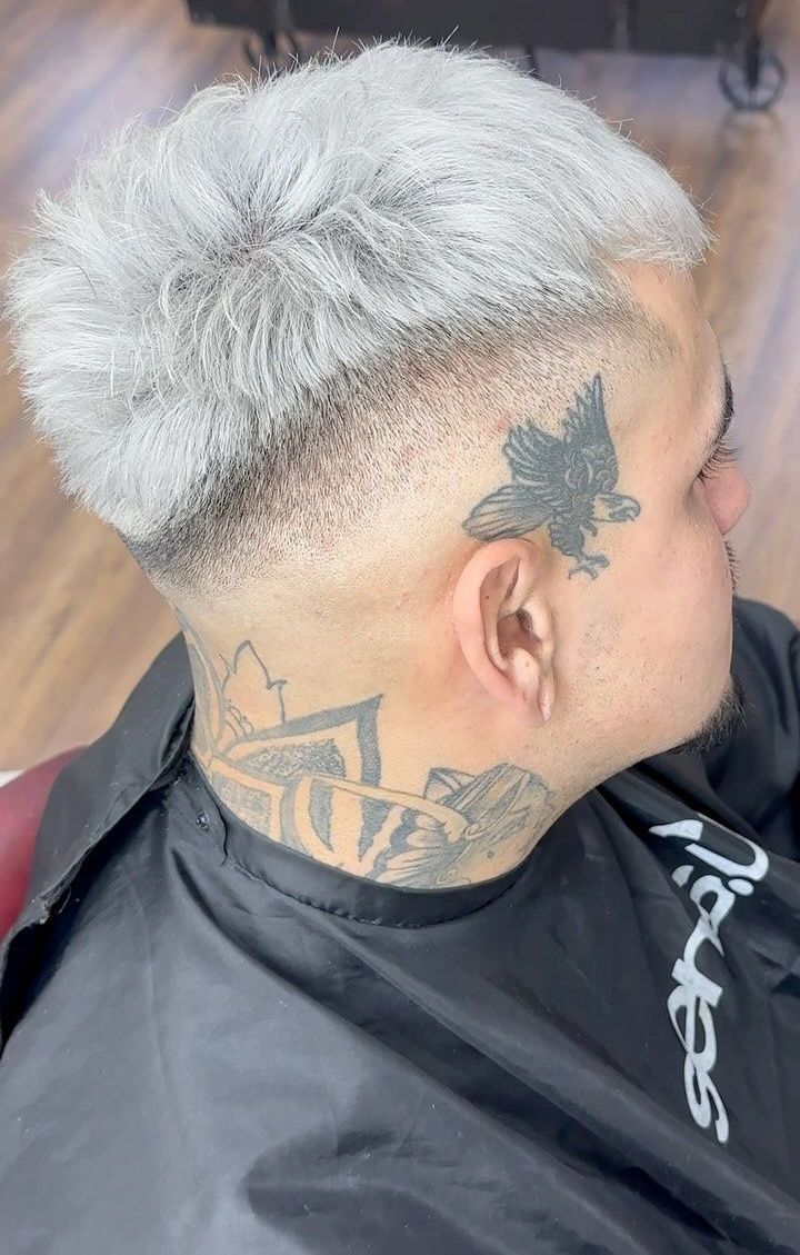 Un hombre con cabello gris y un tatuaje en la cara se está cortando el pelo en una barbería.