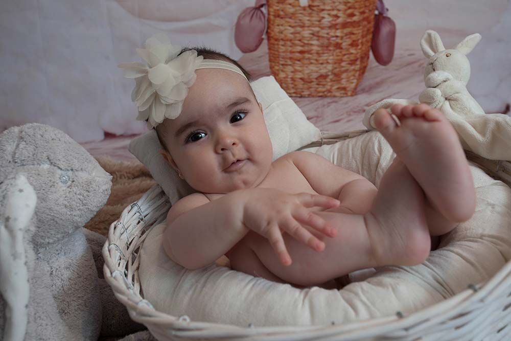 Un bebé está acostado en una canasta con una flor en la cabeza.