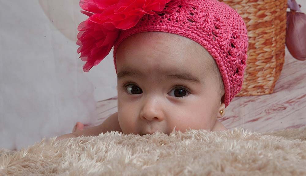 Un bebé que lleva un sombrero rosa está acostado sobre una manta.