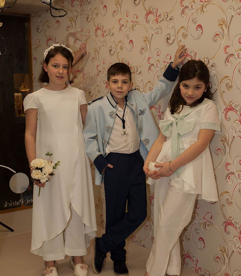 Un niño y dos niñas de pie uno al lado del otro frente a una pared.