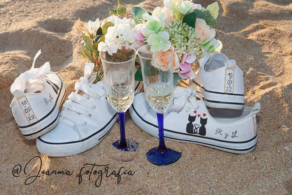 Un par de zapatos de boda y dos copas de vino en la playa.