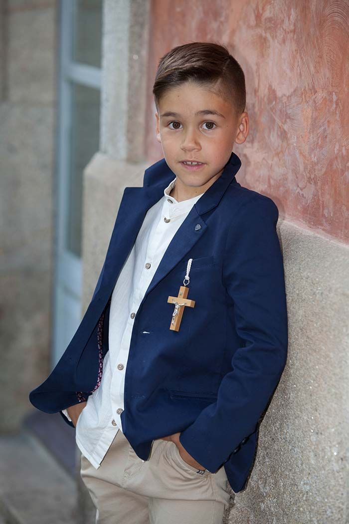 Un niño pequeño que lleva una chaqueta azul y una camisa blanca está apoyado contra una pared.