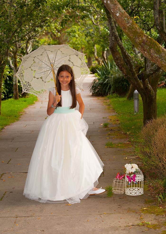 Una niña con un vestido blanco sostiene un paraguas.