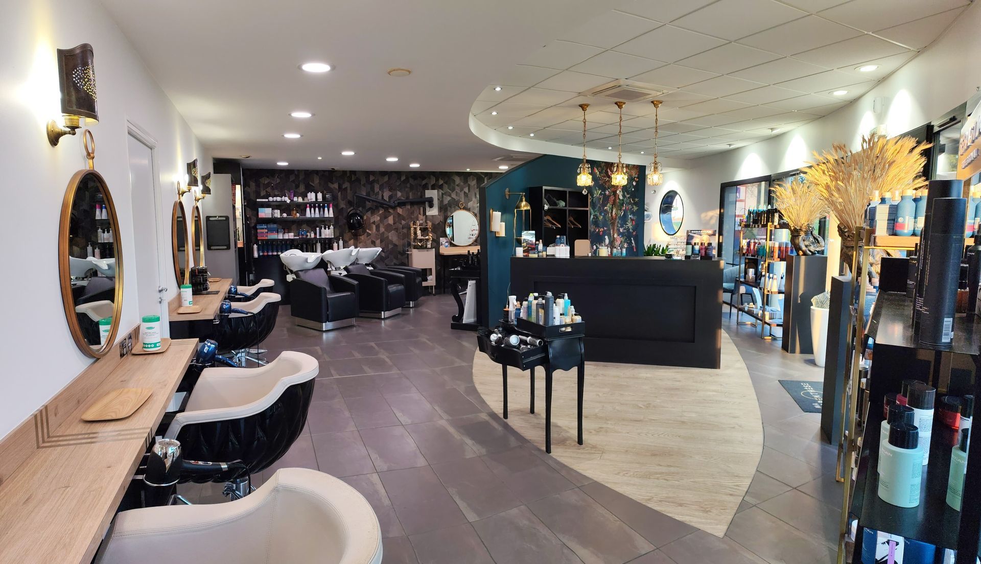Intérieur d'un salon de coiffure : postes de coiffure avec miroirs, présentoirs de produits et un espace d'accueil.