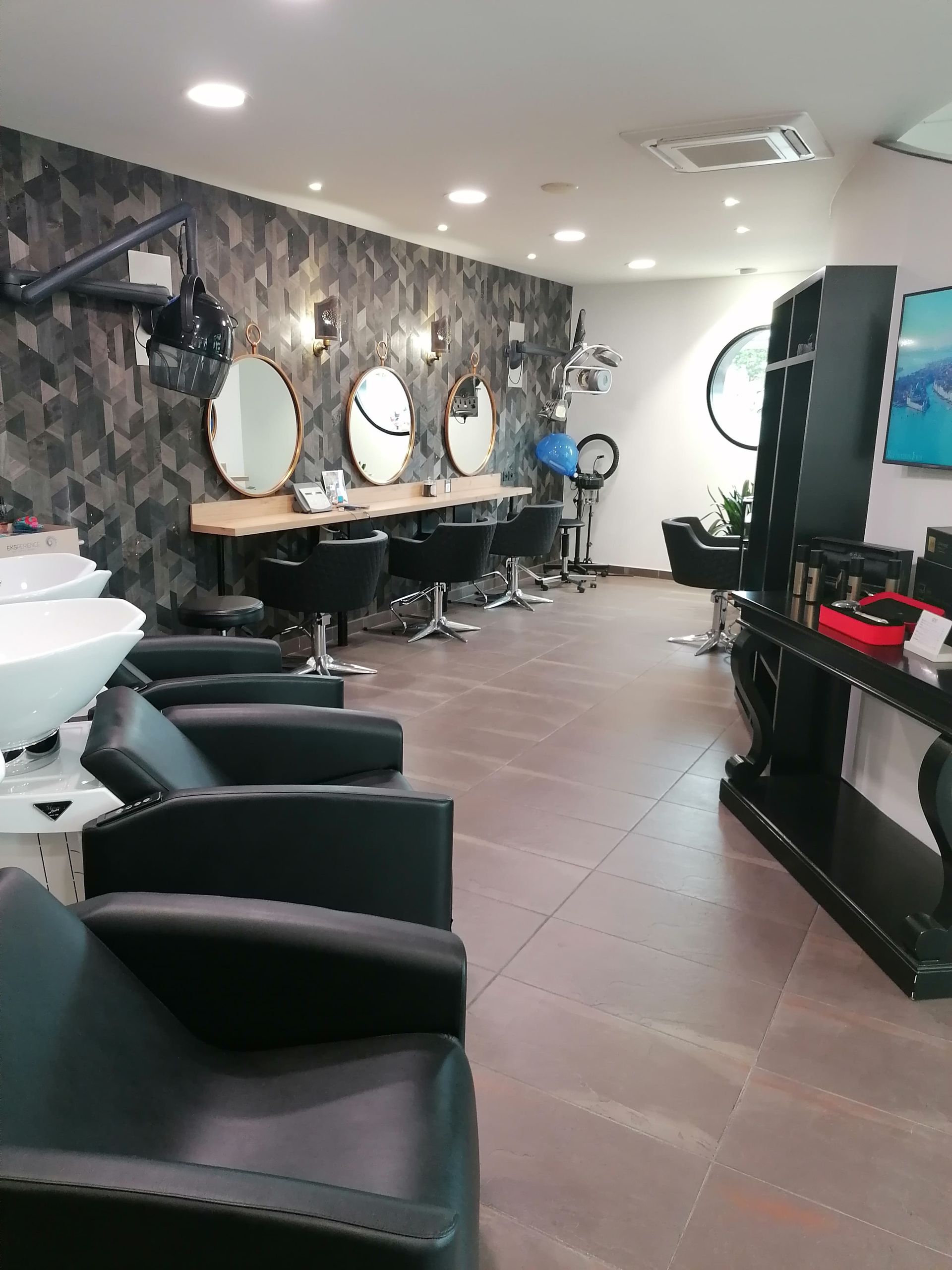 Intérieur d'un salon de coiffure avec chaises noires, miroirs et postes de travail.