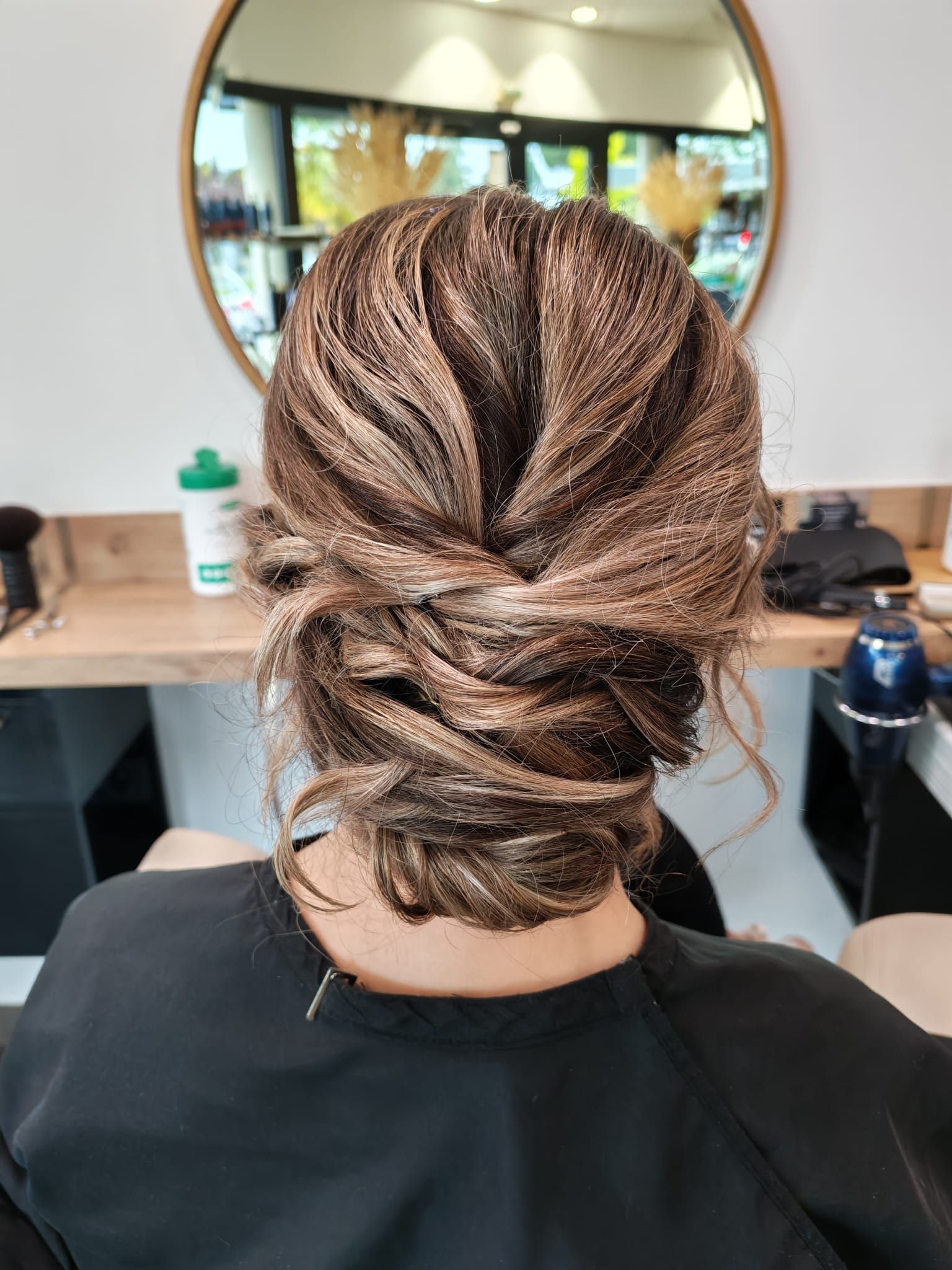 Femme coiffée d'un chignon brun et blond, dans un salon de coiffure. Cheveux torsadés et volumineux.