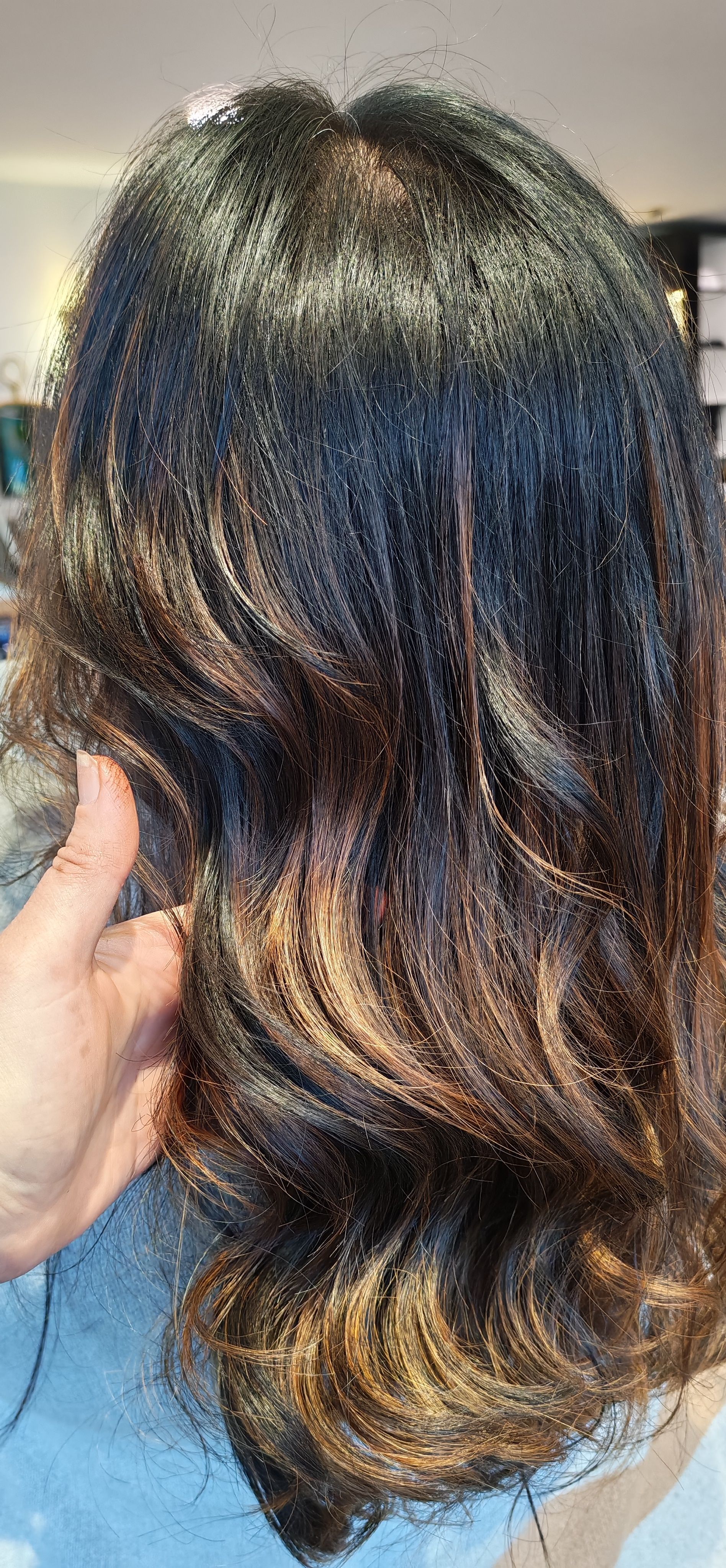 Cheveux ondulés foncés avec des mèches éclaircies. Une main tient les cheveux.