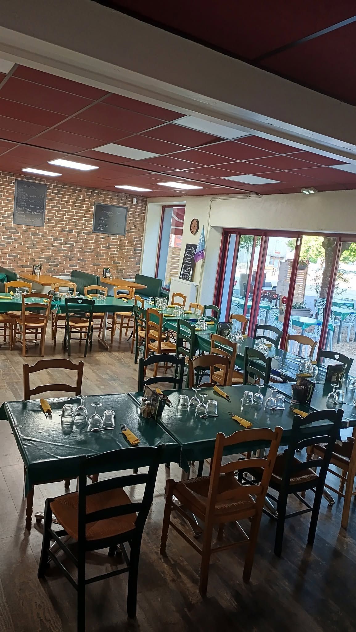 Salle à manger de restaurant vide avec tables et chaises en bois, panneaux de plafond rouges et grandes fenêtres.