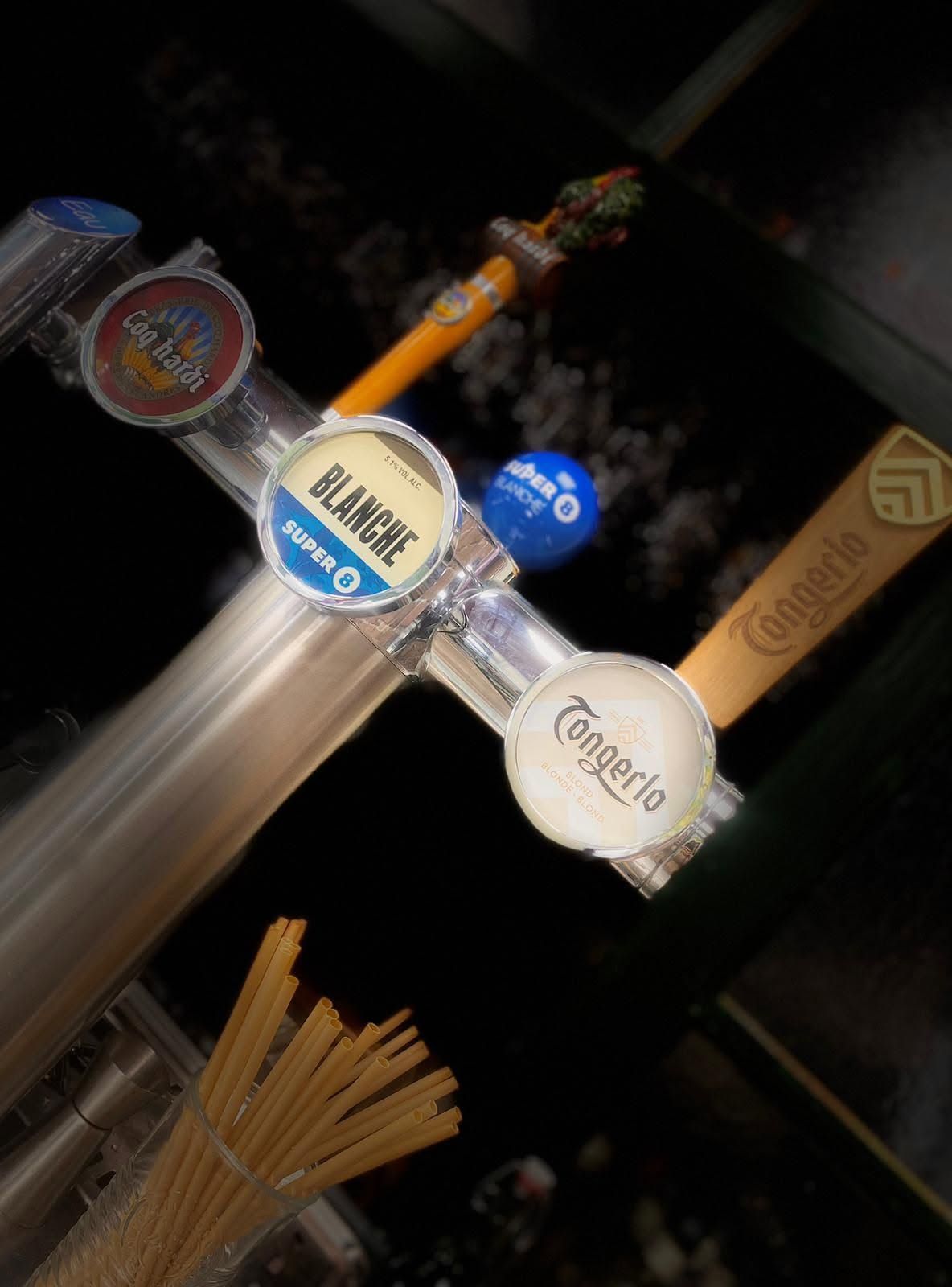 Poignées de tireuses à bière dans un bar à l'ambiance tamisée, avec un seau de bretzels en dessous.