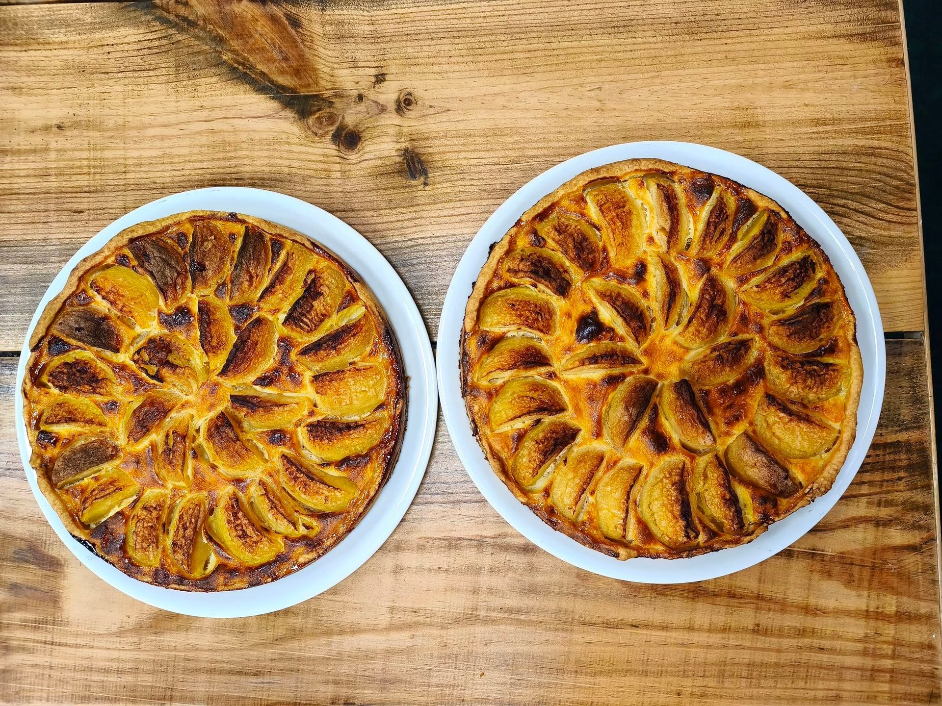 Deux pâtisseries dorées cuites au four dans des plats blancs sur une table en bois.
