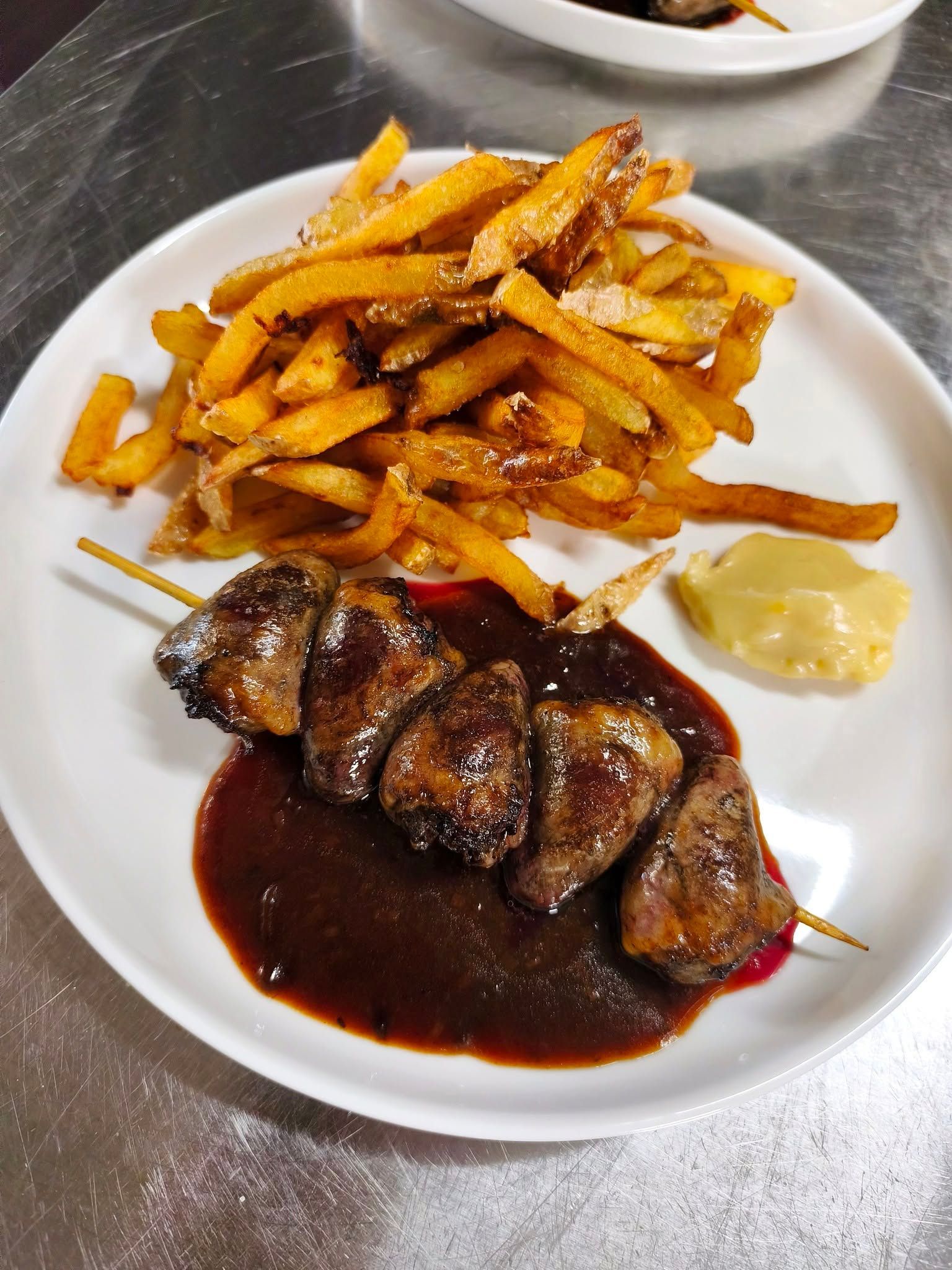 Assiette de steak avec sauce brune et une montagne de frites dans un plat blanc, sur une table en métal.
