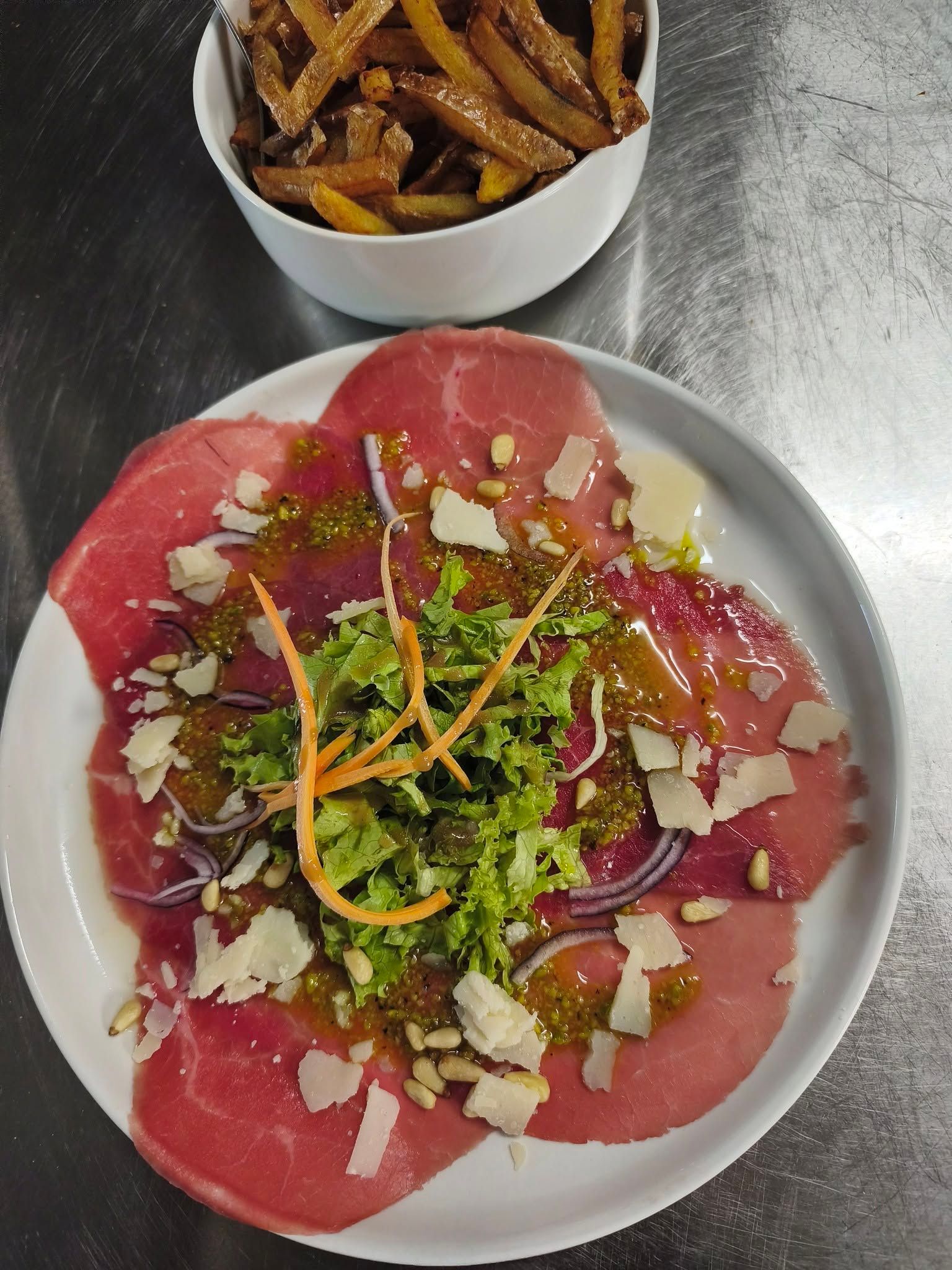 Carpaccio de betteraves garni de verdure et de fromage râpé, avec un bol de frites en arrière-plan.