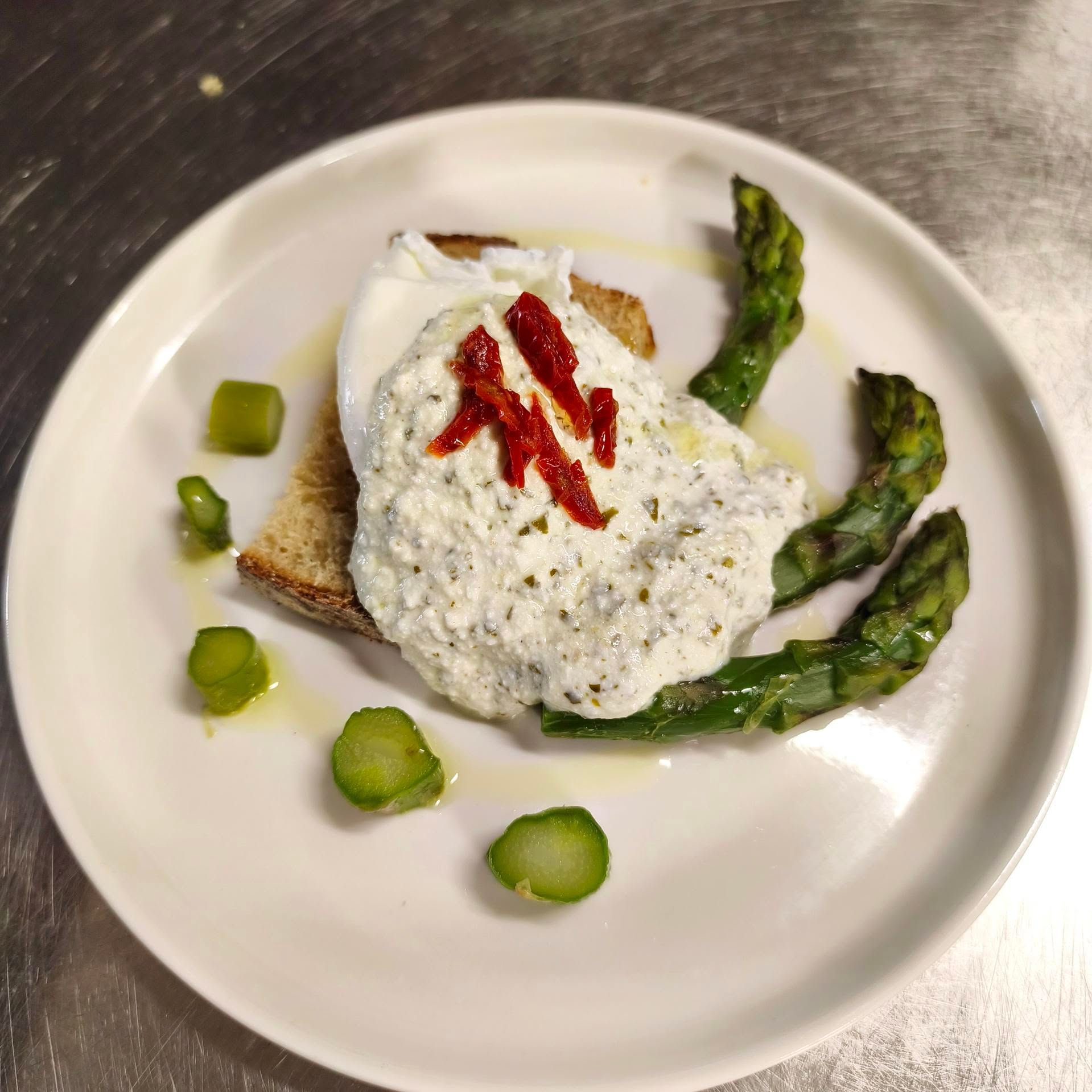 Tartine de pain grillé recouverte de ricotta blanche, garnie de lanières de poivron rouge et d'asperges, servie sur une assiette blanche.