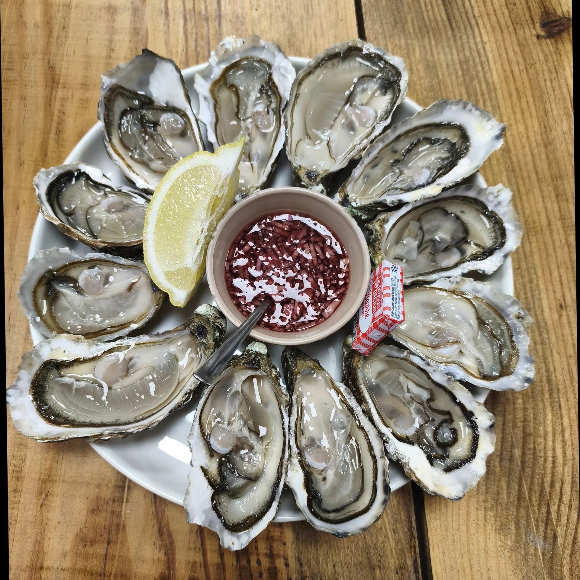 Assiette d'huîtres crues disposées autour de quartiers de citron et de sauce cocktail sur une table en bois.
