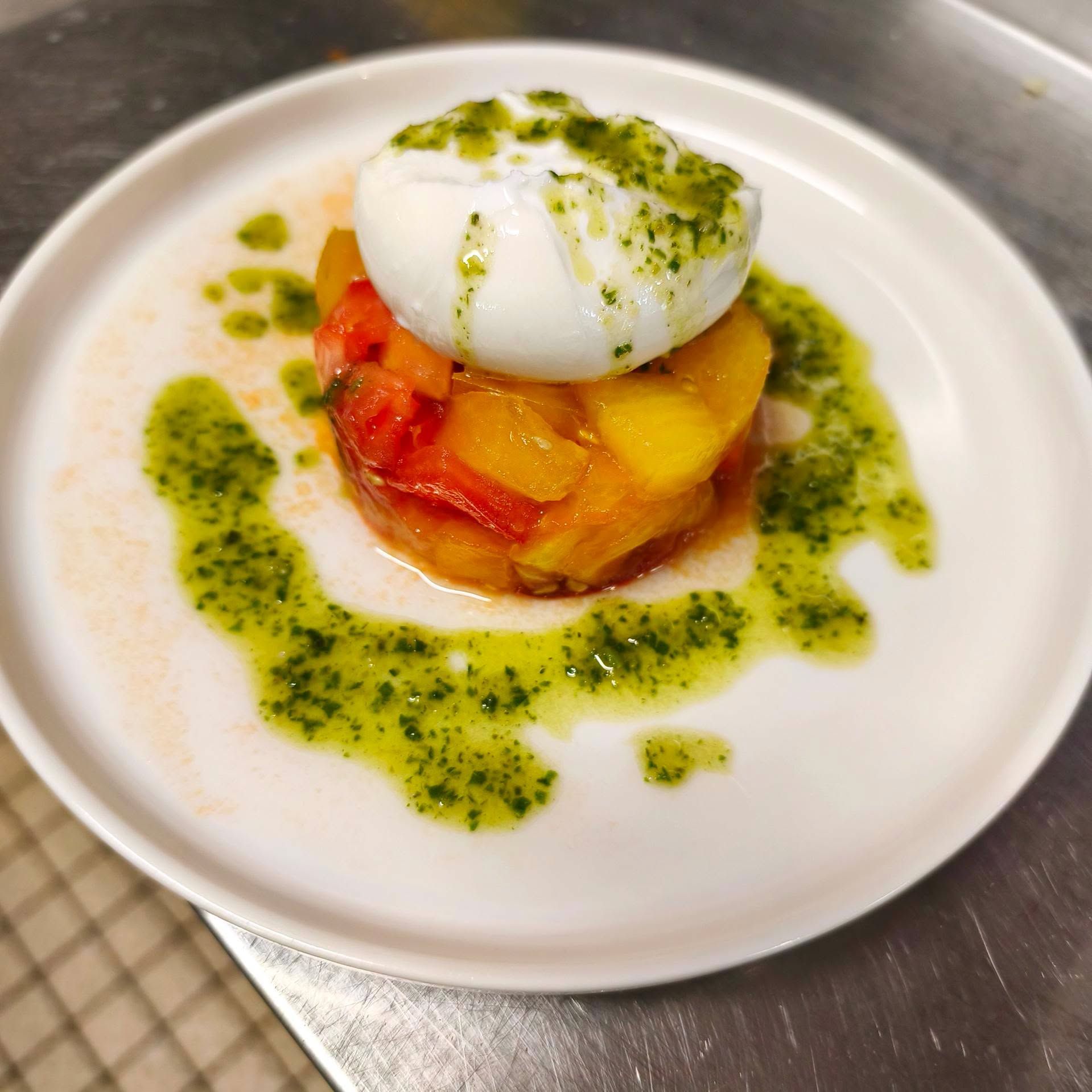 Plat composé d'un œuf poché sur une compotée de légumes, arrosée d'une sauce verte et servie sur une assiette blanche.