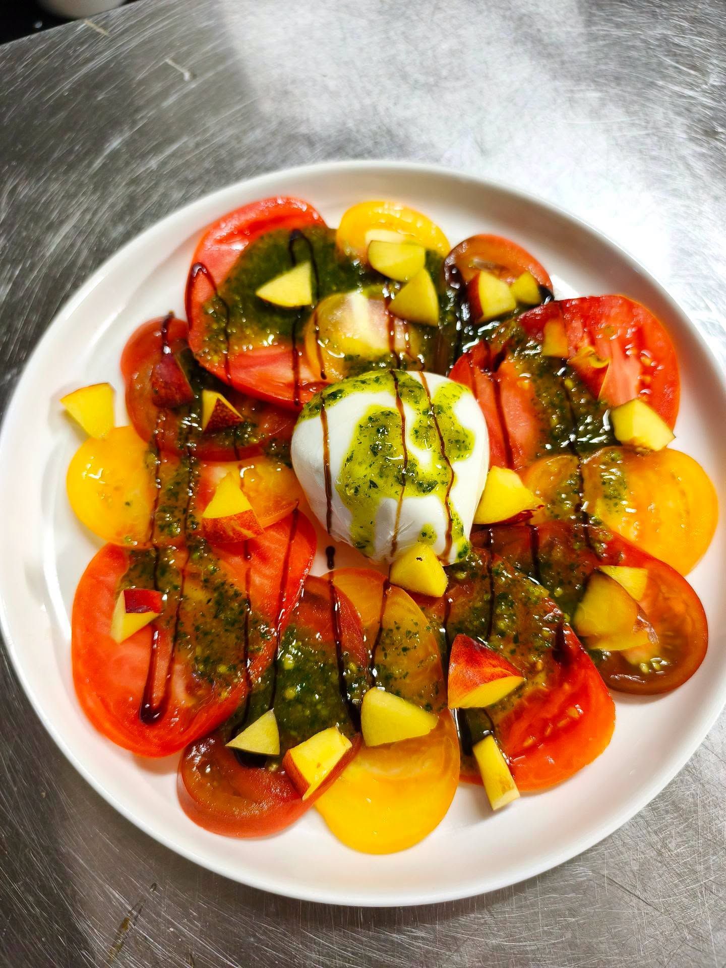Salade de tomates colorées avec mozzarella, basilic et filet de vinaigre balsamique sur une assiette blanche.