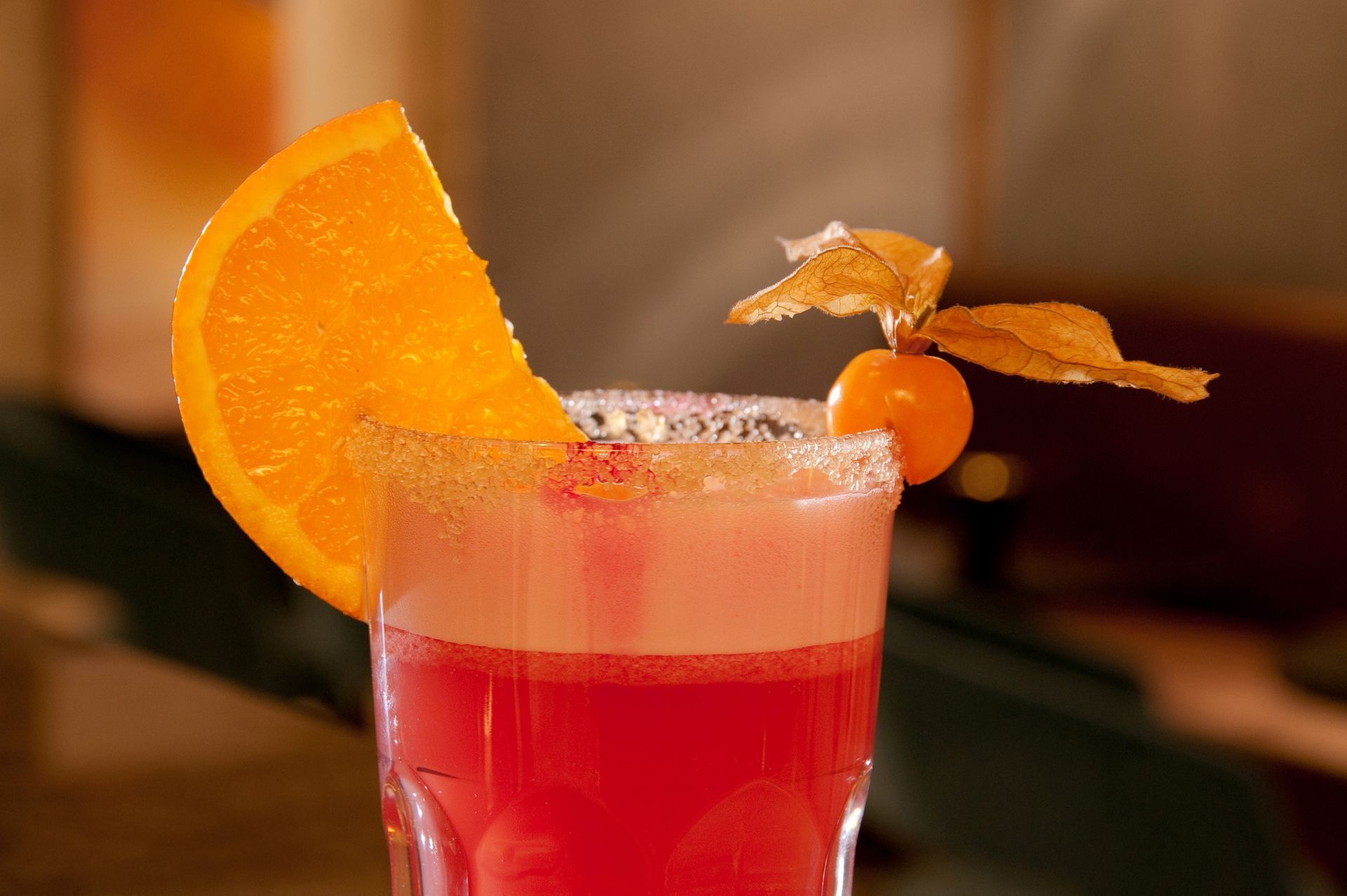 Cocktail rose avec une tranche d'orange, une cerise en garniture et une fleur dans un verre à pied.