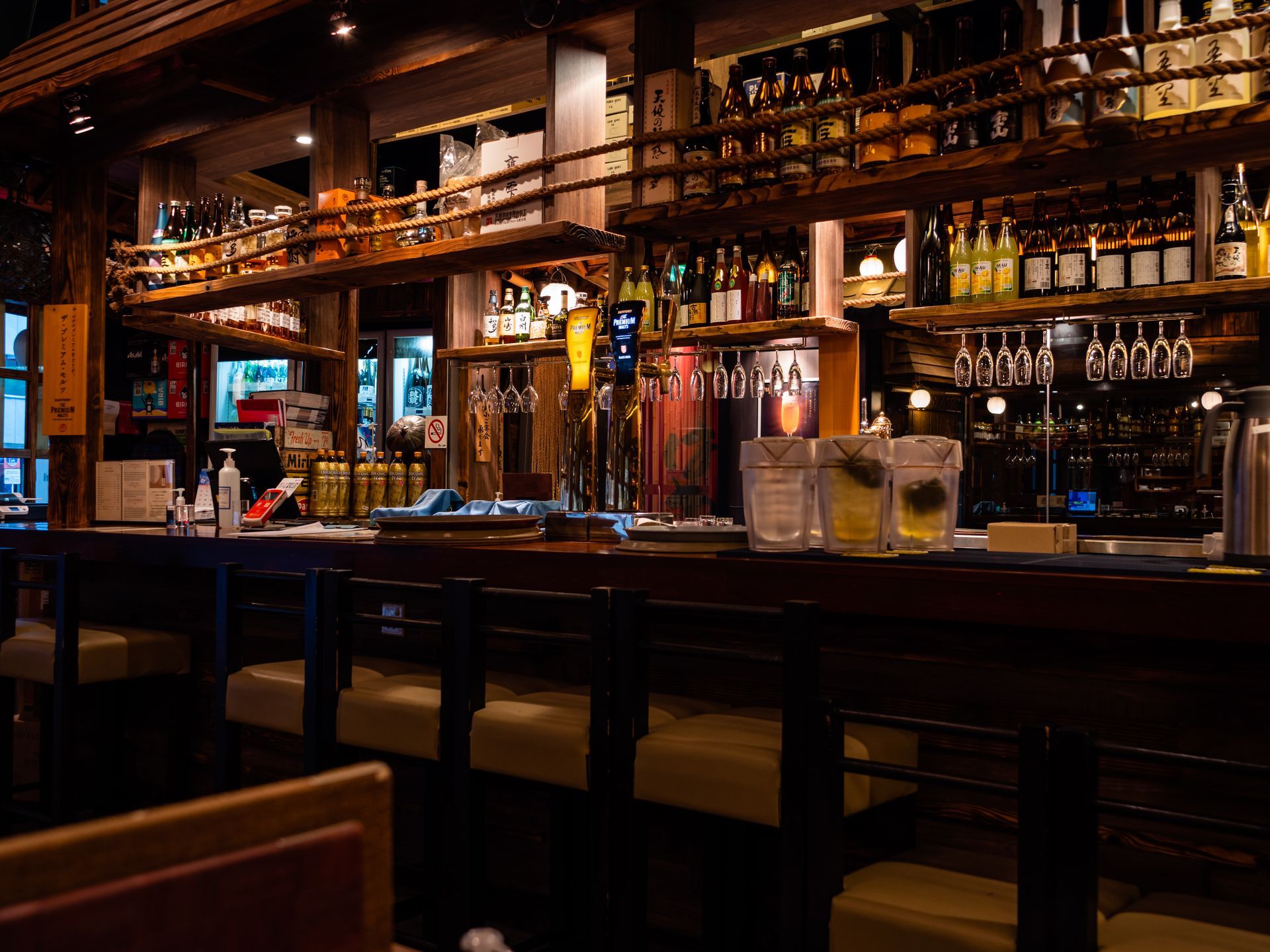 Intérieur de bar à l'éclairage tamisé, avec des étagères de bouteilles d'alcool, des tabourets et un comptoir en bois poli.